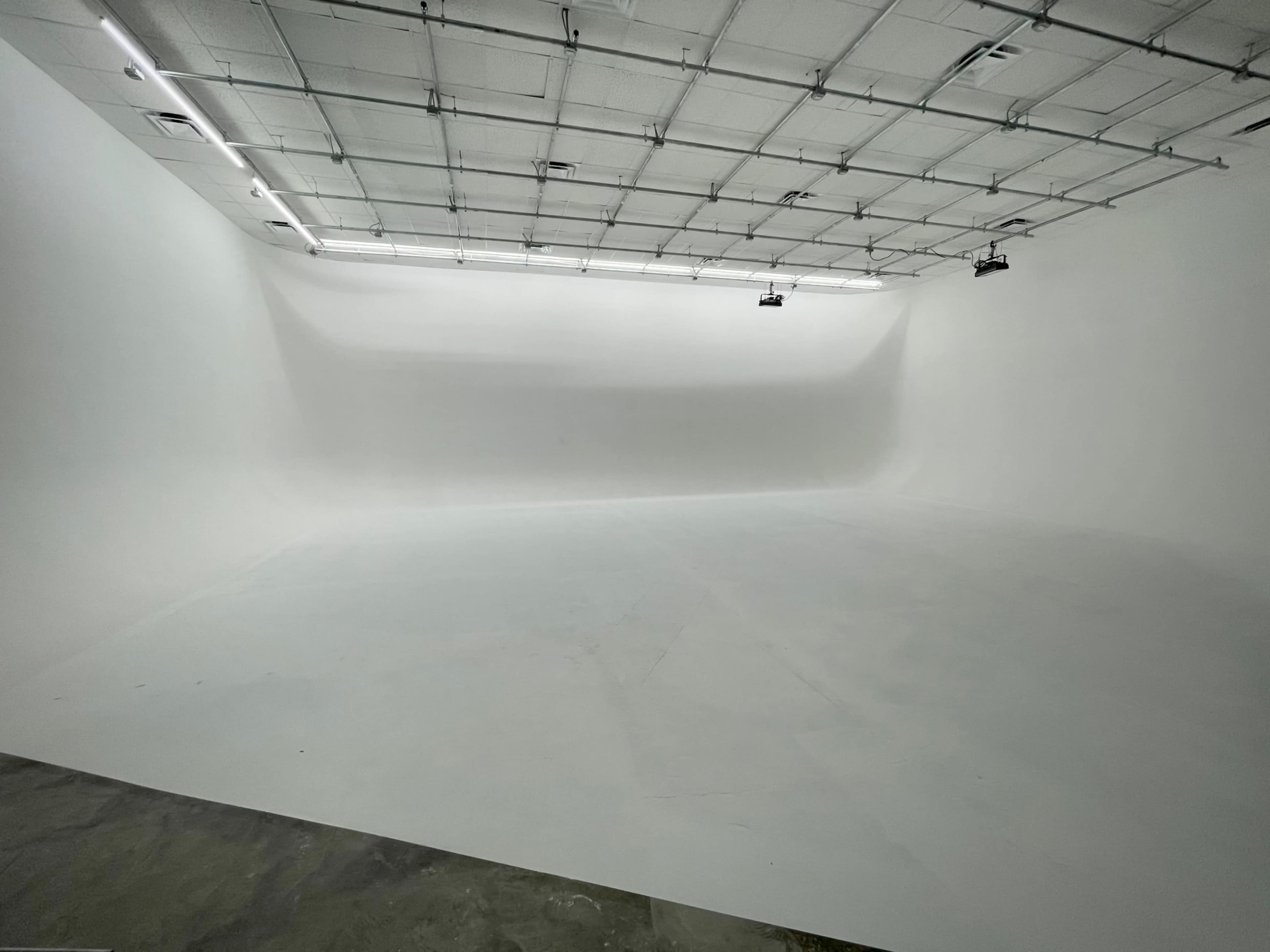 A large, empty studio space with white walls and a smooth floor under bright overhead lighting.
