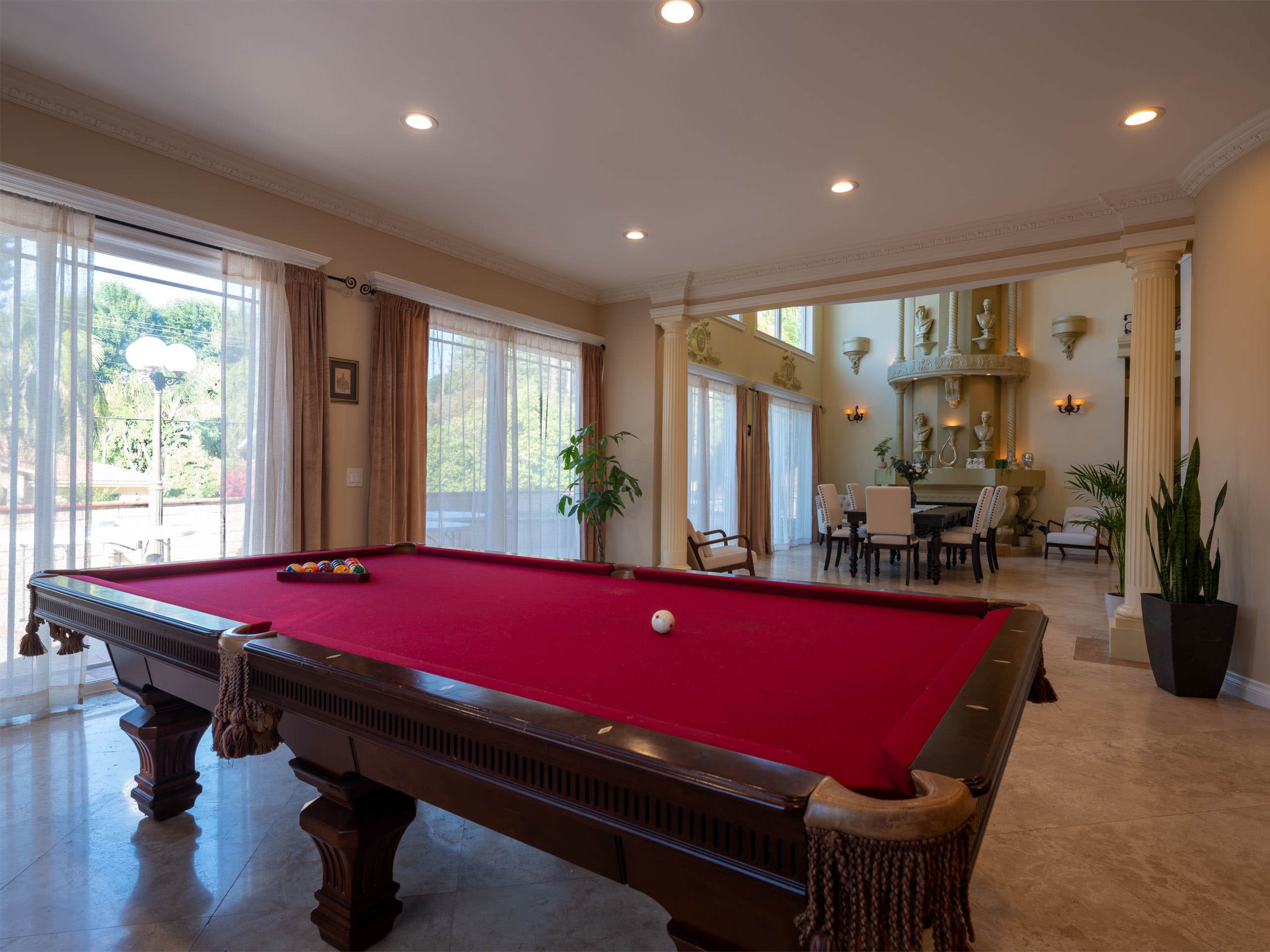 The image shows a spacious living area with a red pool table in the foreground and a dining area visible in the background.