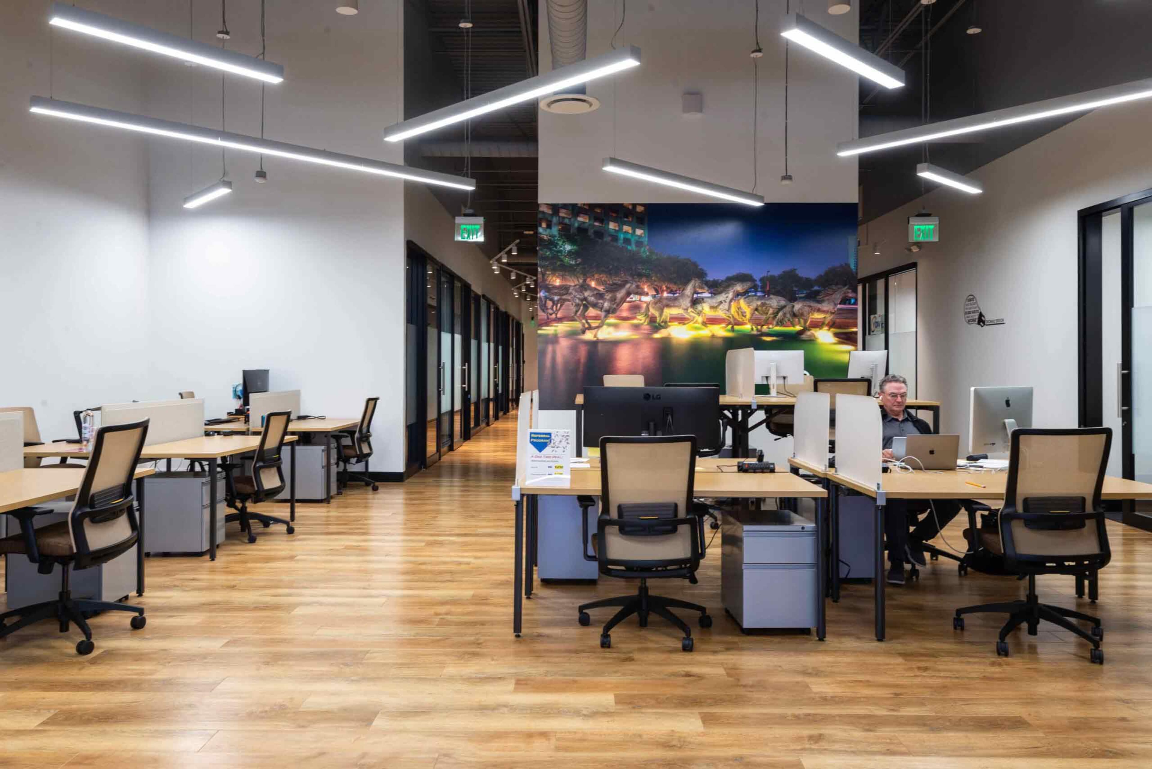 The image shows an open office space with several workstations and a large mural of a cityscape on the wall.