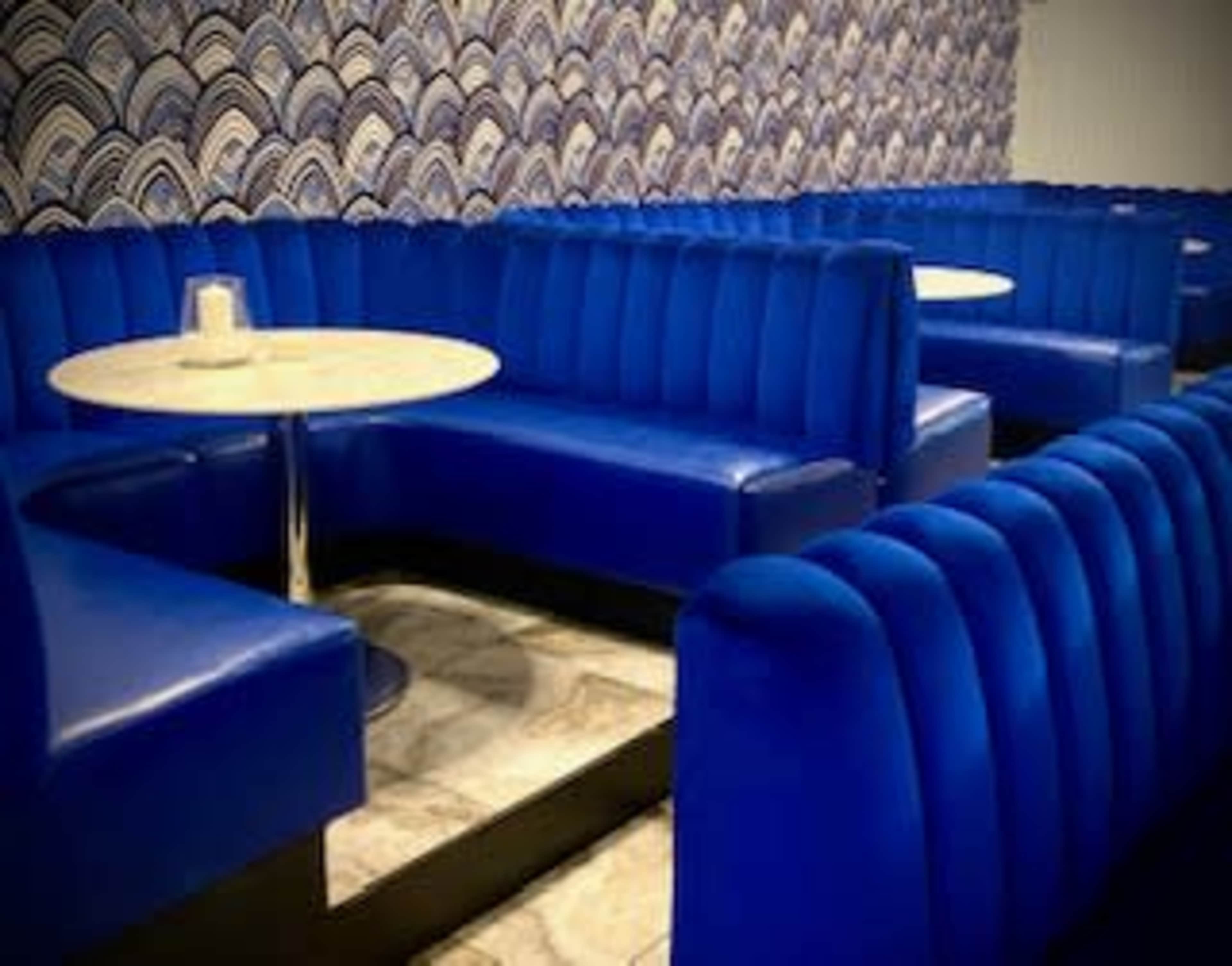 The image shows a restaurant interior with blue upholstered booths and circular tables against a patterned wall.