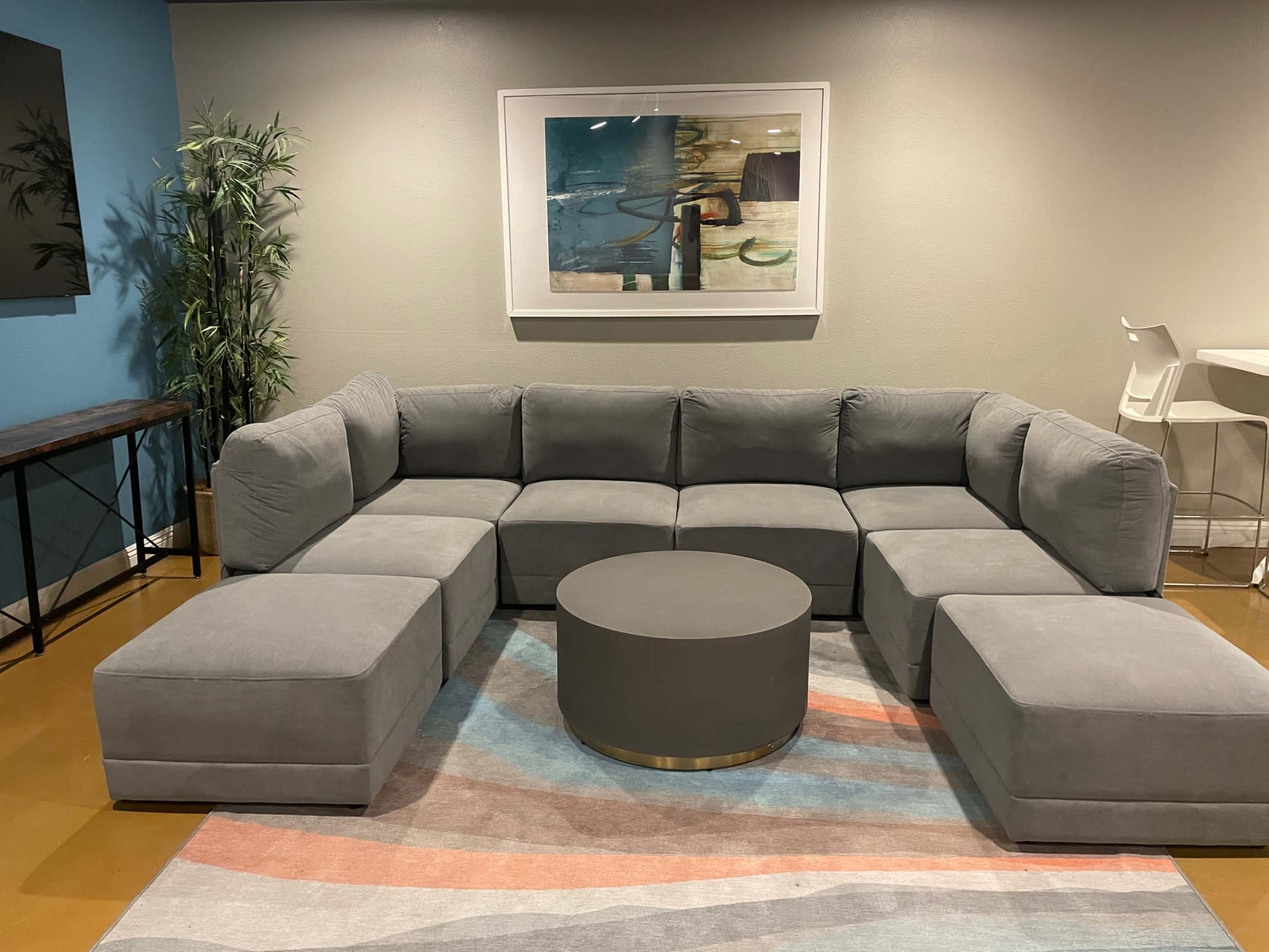 A modern gray sectional sofa arranged around a circular coffee table on a striped area rug in a well-lit room.
