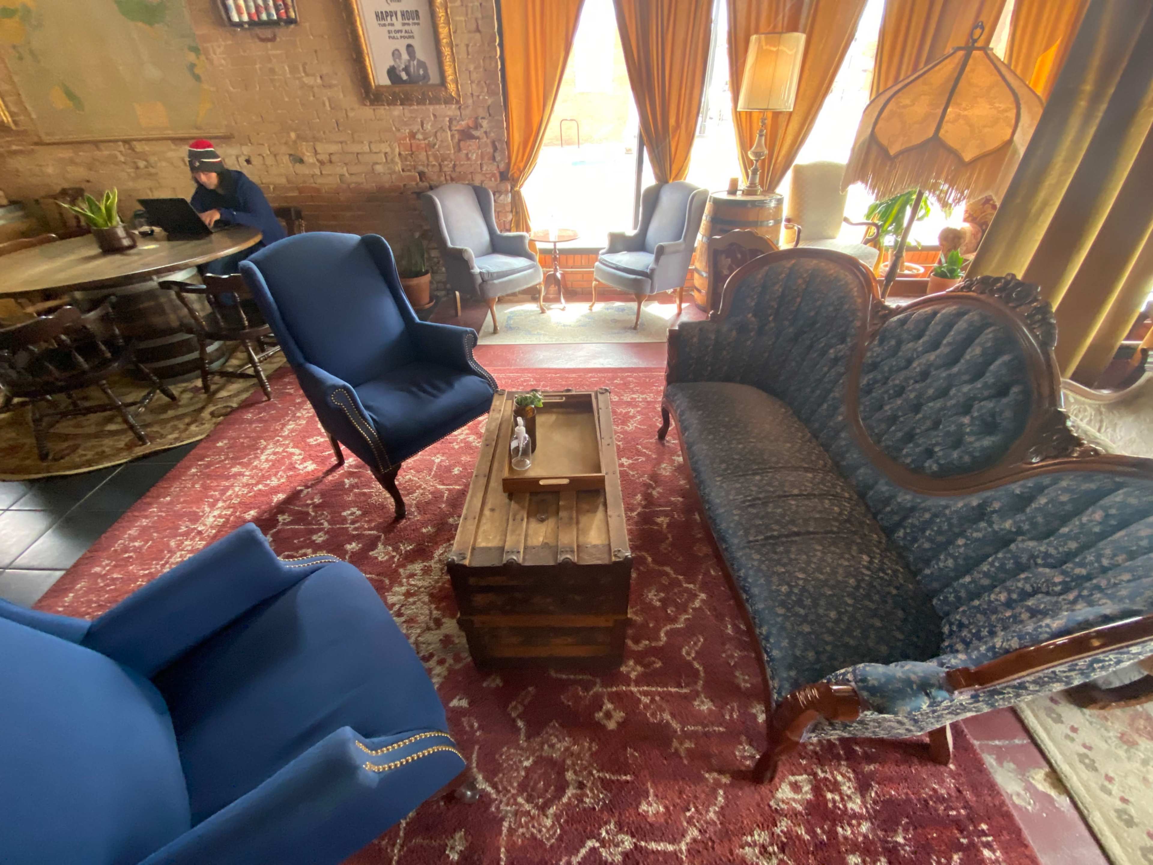 A cozy indoor seating area with vintage blue sofas and chairs, a wooden coffee table, and large windows adorned with curtains.