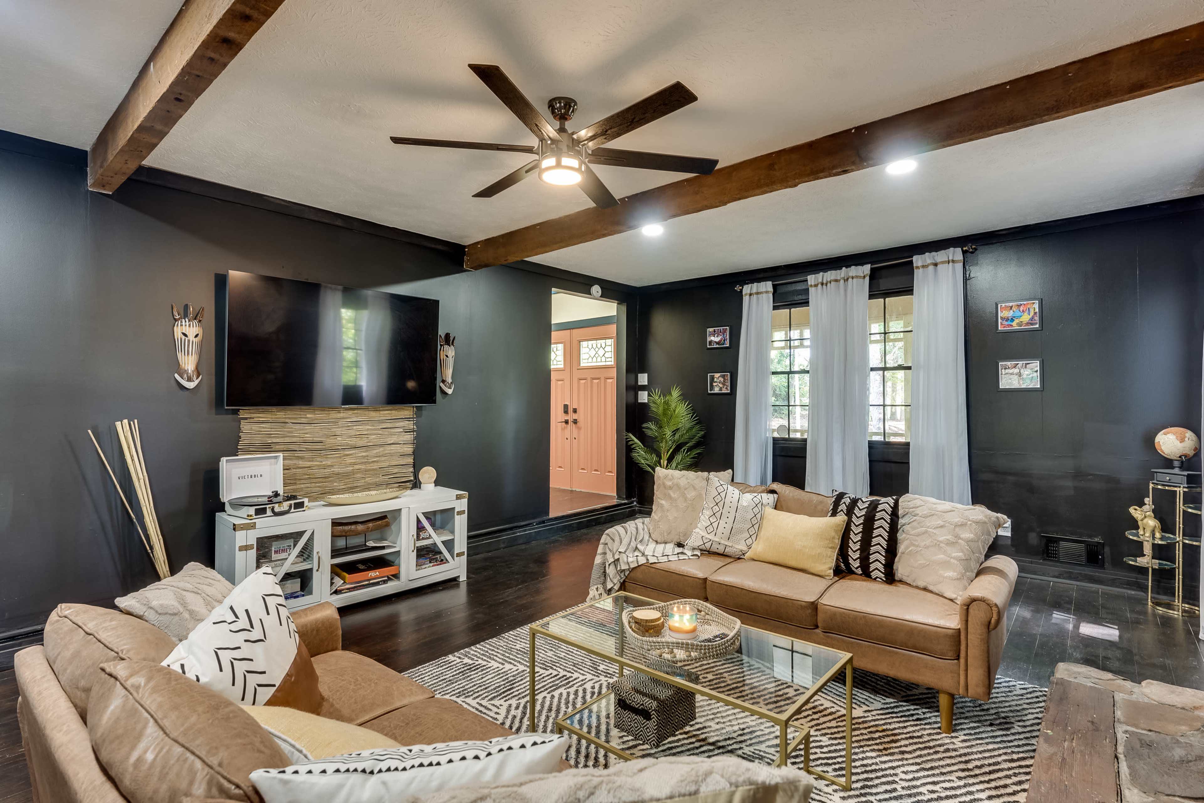 A modern living room features two sofas, a coffee table, a mounted television, and a decorative wall with wood beams and a door leading outside.