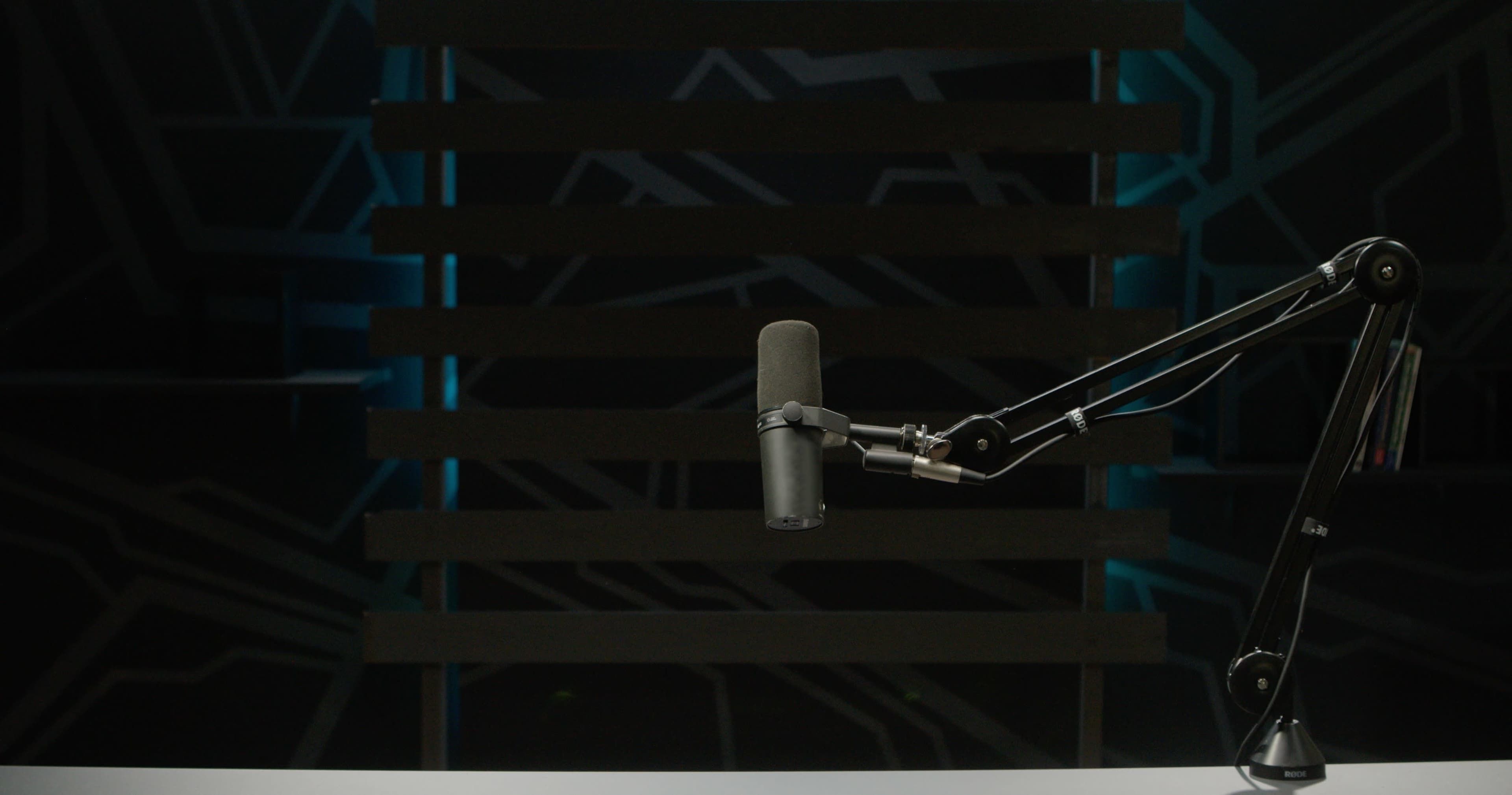 A microphone mounted on an adjustable arm is positioned on a plain table in front of a dark, geometric backdrop.