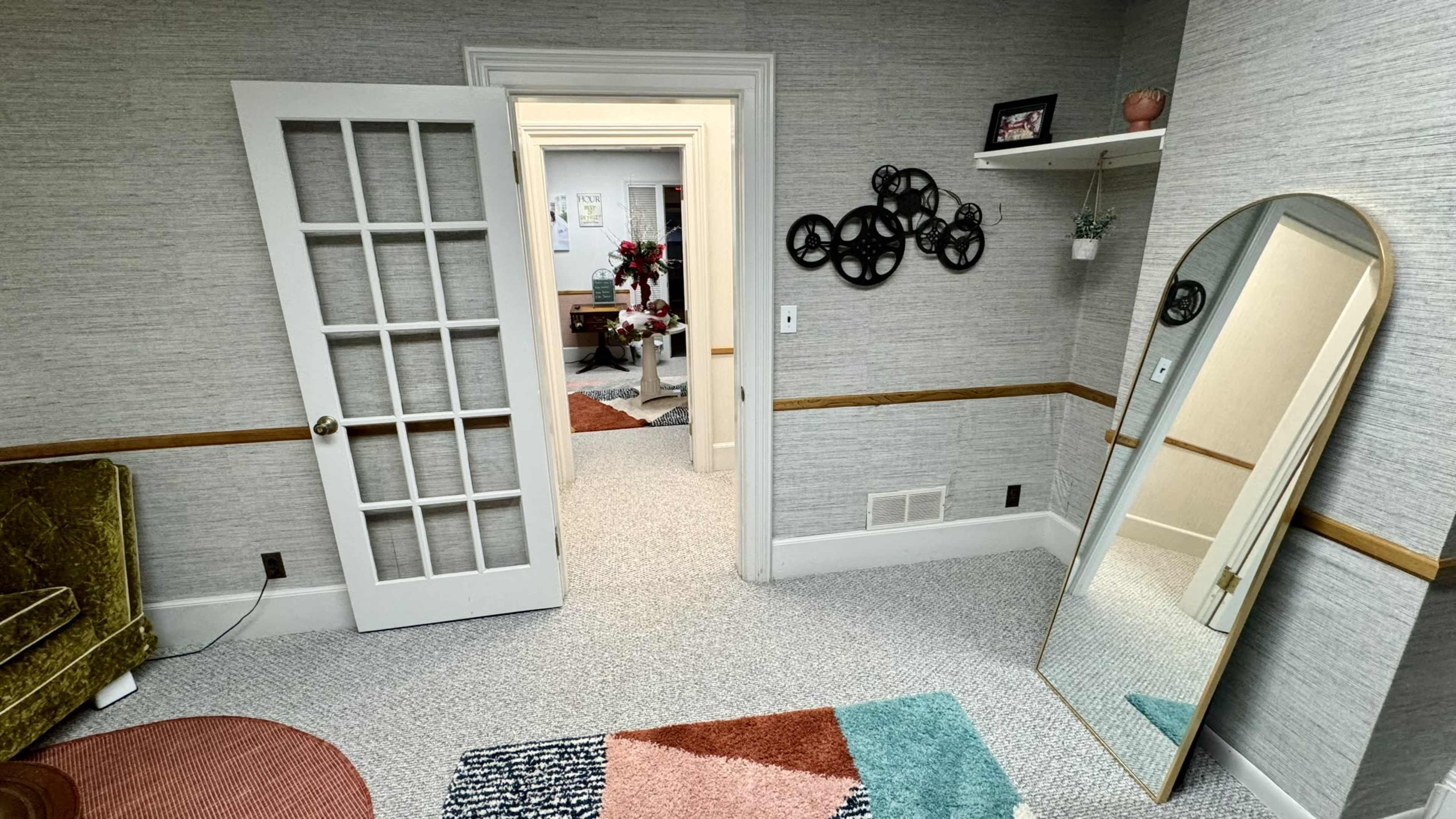 The image shows a softly lit room with a green velvet couch, an ornate mirror, and a doorway leading to another room, all accented by patterned rugs and decorative wall elements.