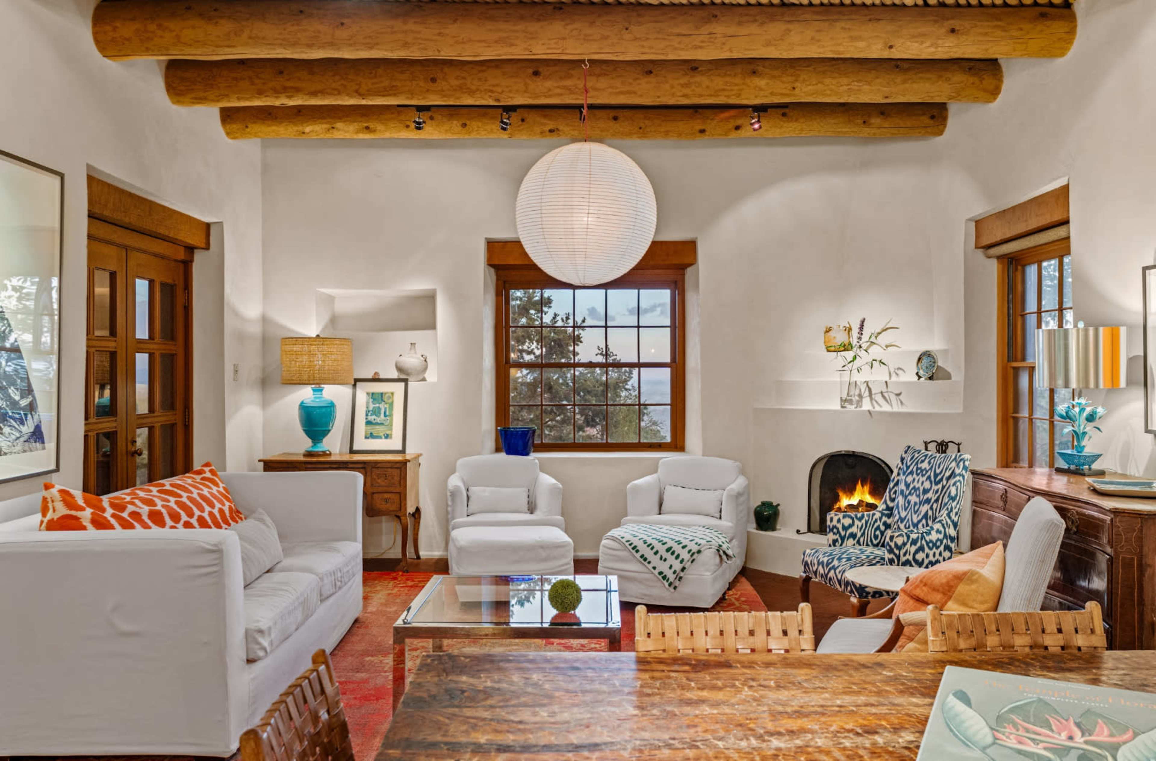 The living room features white furniture, a wooden table, a cozy fireplace, and large windows with a view.
