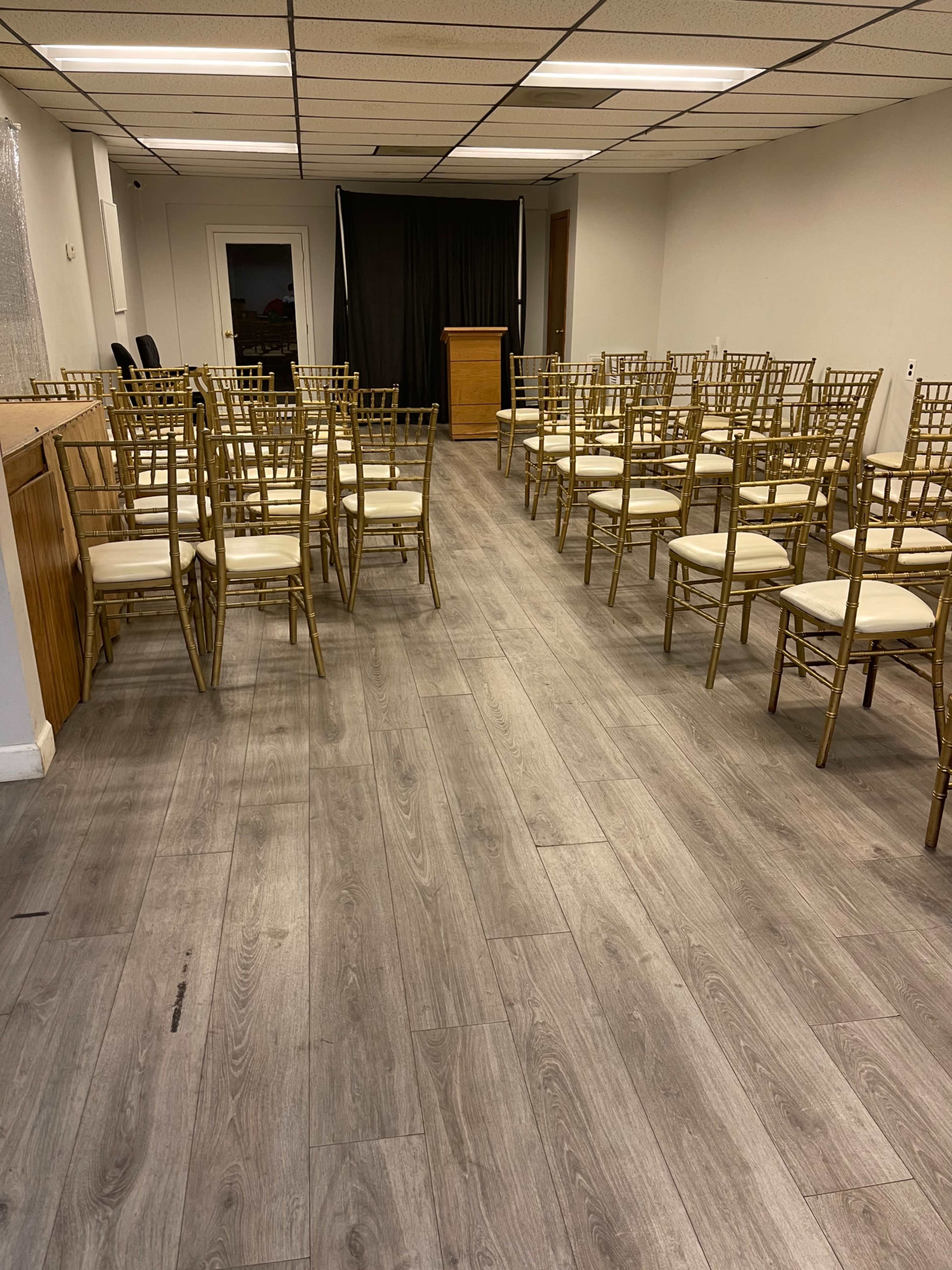 A room features a row of gold chairs with cushions arranged facing a podium, set against a backdrop of black fabric.