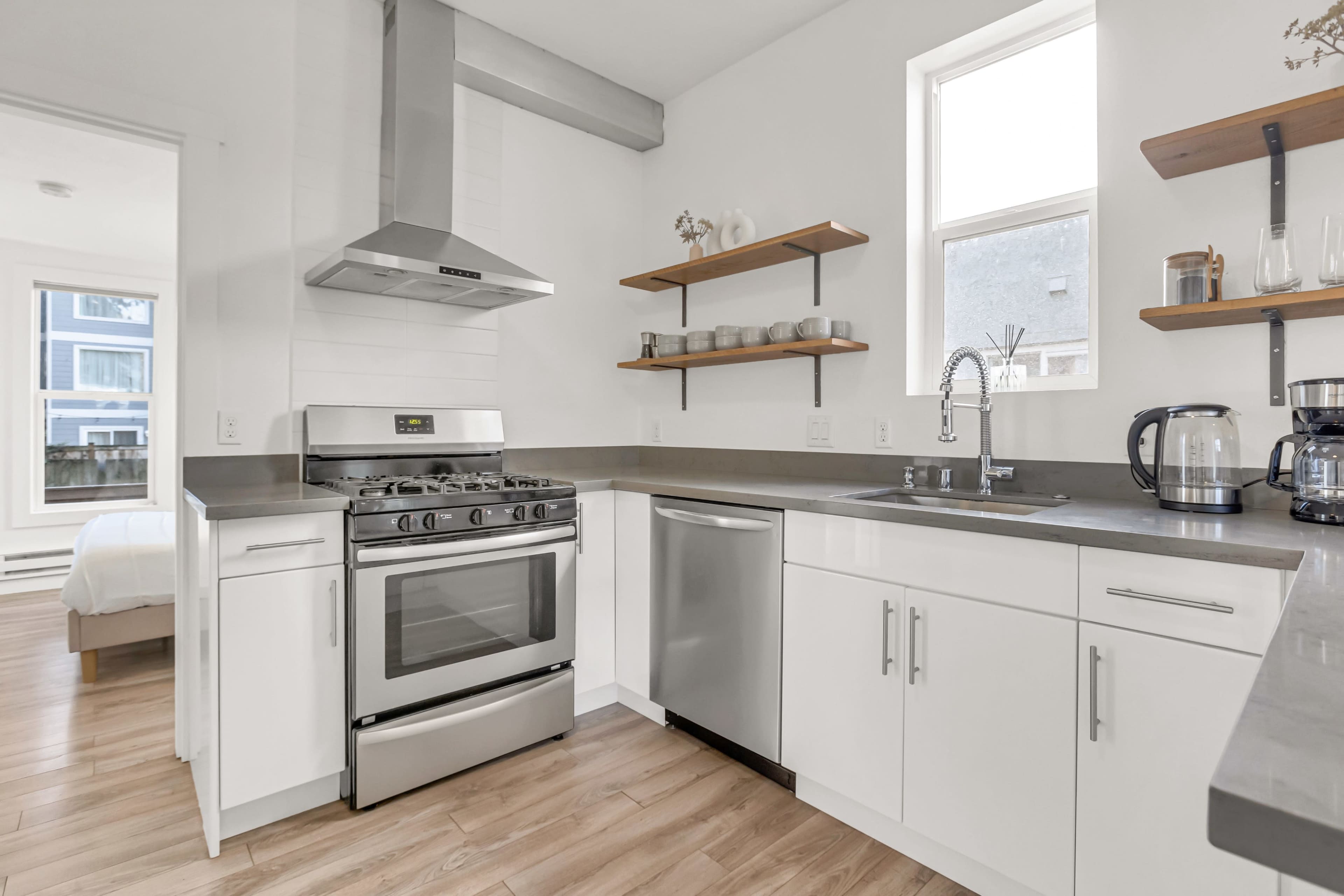 The image shows a modern kitchen with stainless steel appliances, white cabinetry, and wooden shelving.