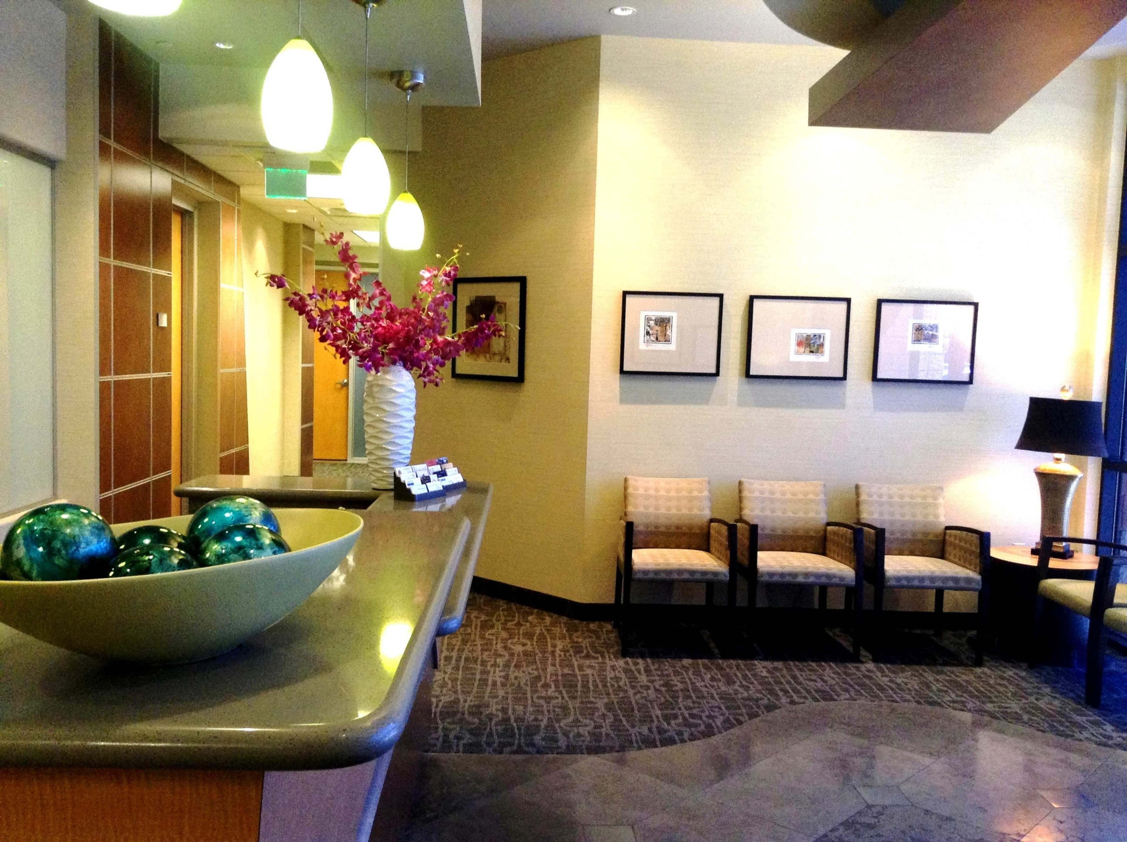 A modern reception area with a curved counter, decorative flowers, and two rows of chairs along the wall.