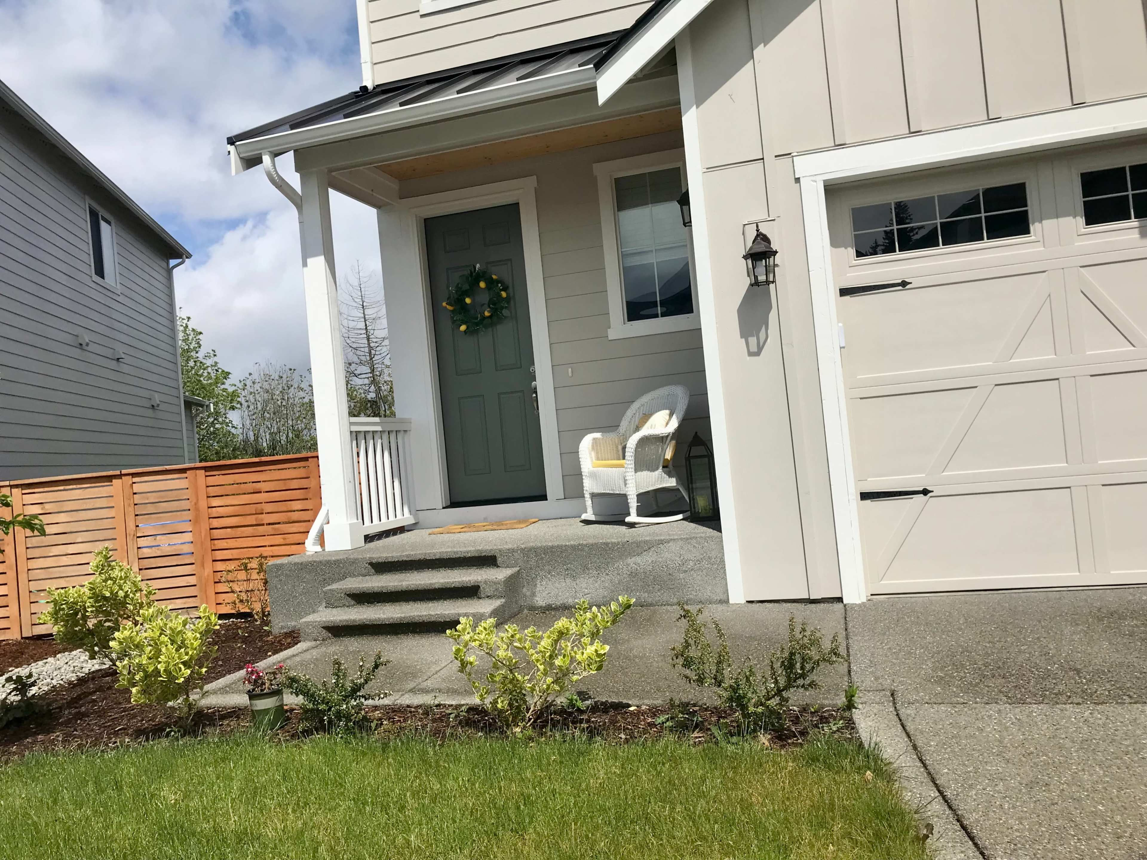 The exterior of a house with a front porch, steps leading to a green door, and a couple of white chairs on the porch.