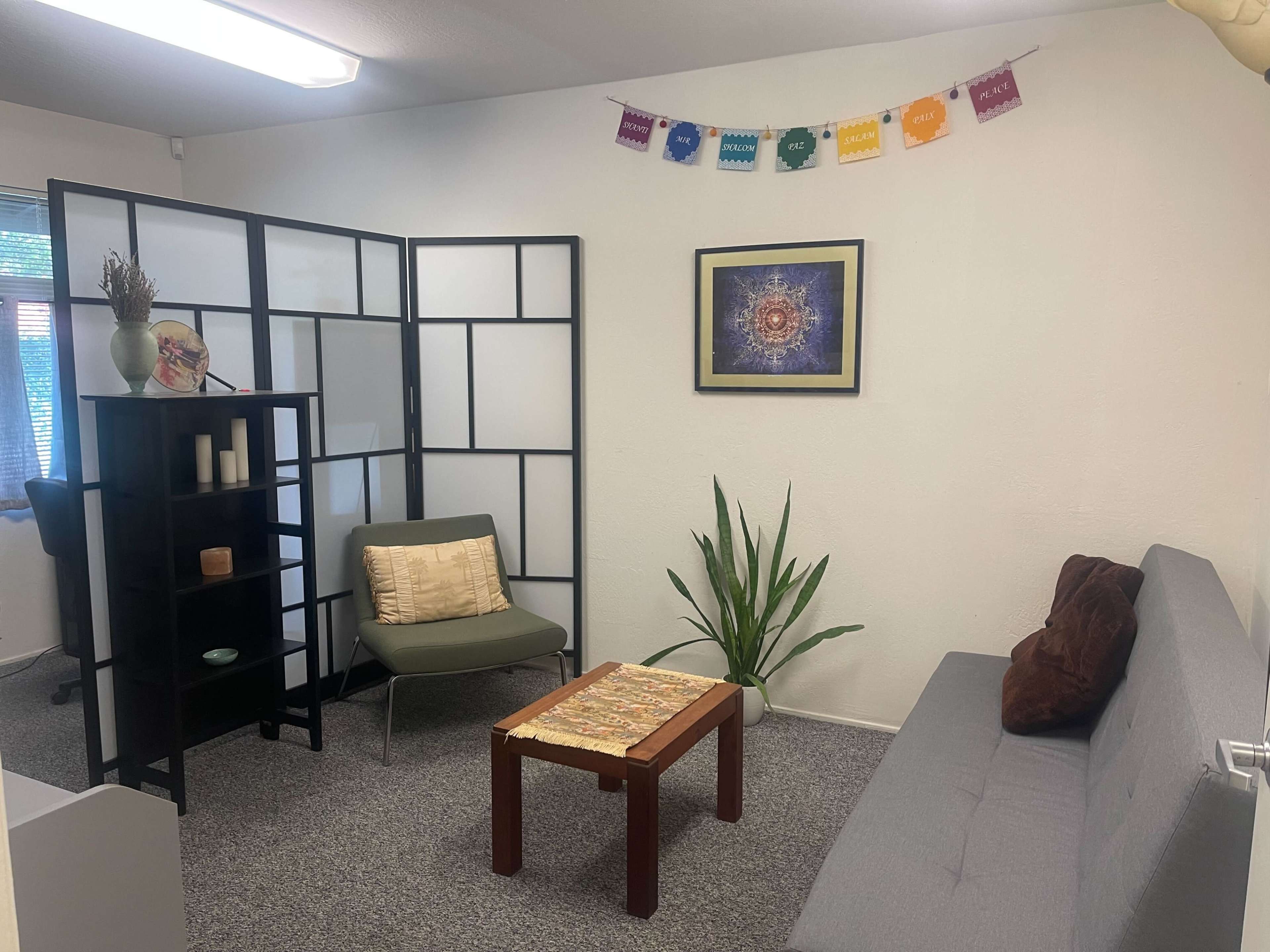A small room with a seating area featuring a gray couch, a green chair, a wooden coffee table, and decorative elements on the walls.