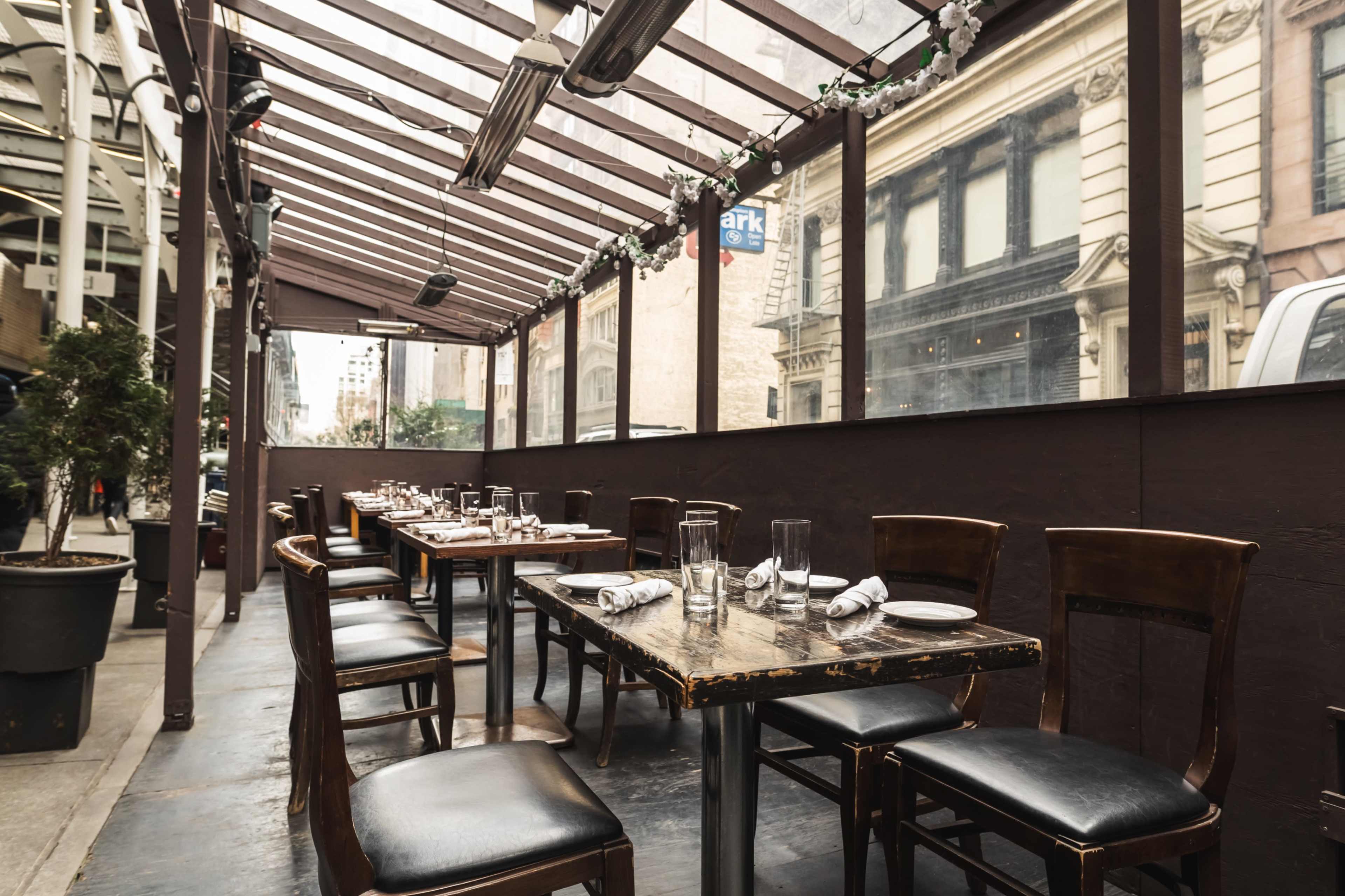 A covered outdoor dining area features several tables arranged with chairs and empty glassware.