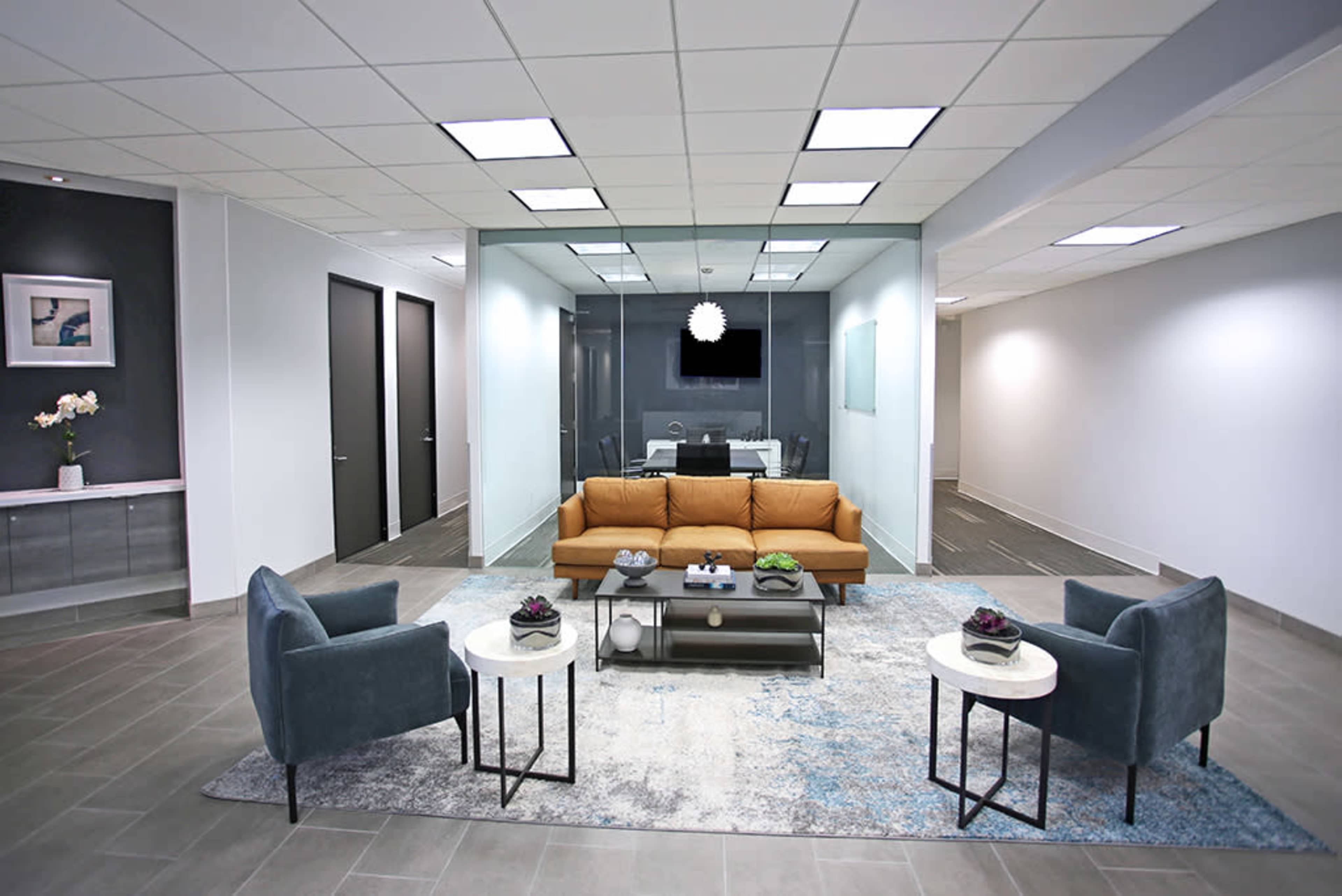 A modern office reception area with a brown sofa, two blue armchairs, and a coffee table centered on a patterned rug.