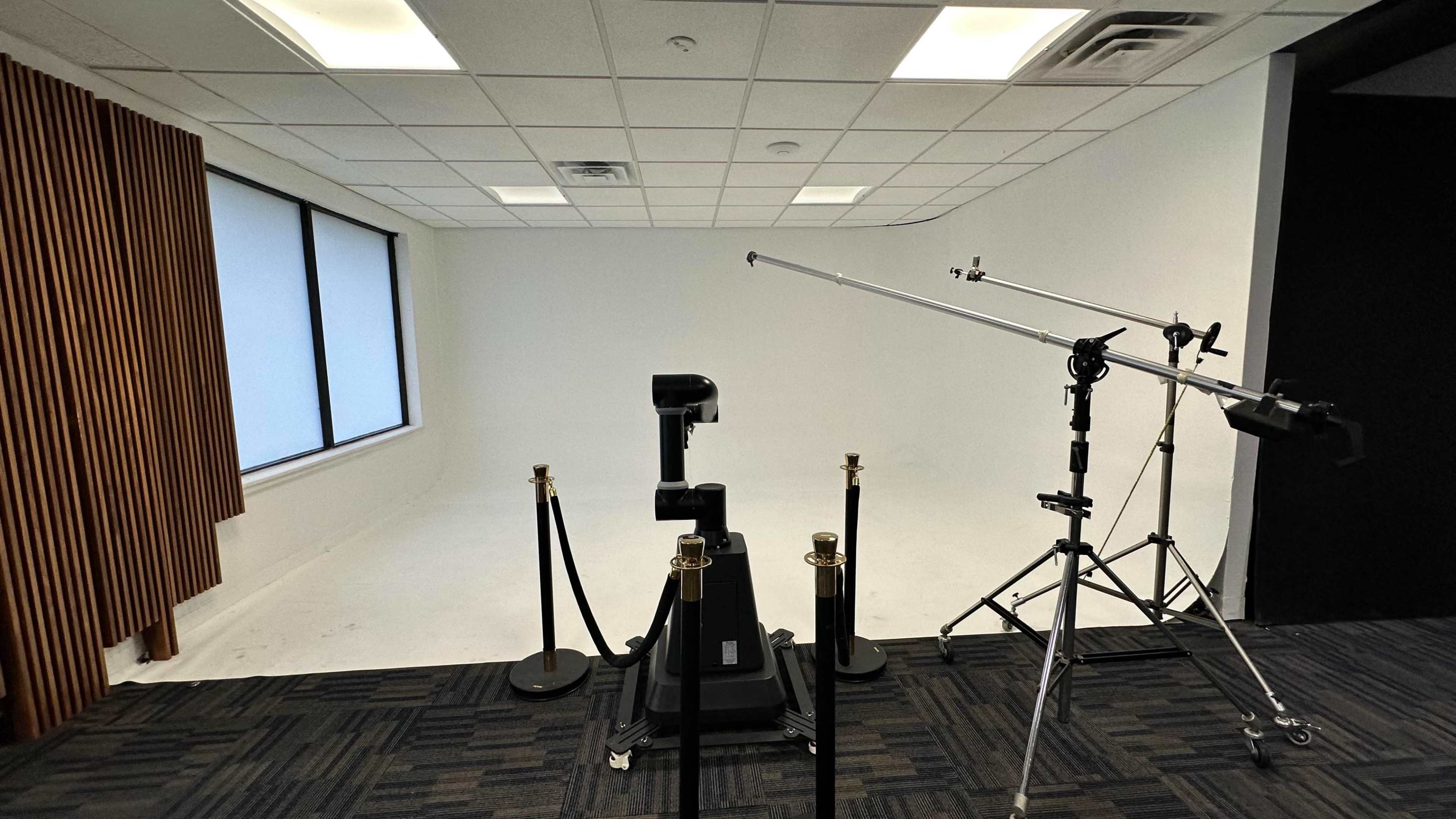 The image shows an empty studio space with a robotic arm, a boom mic stand, and a barrier of stanchions.