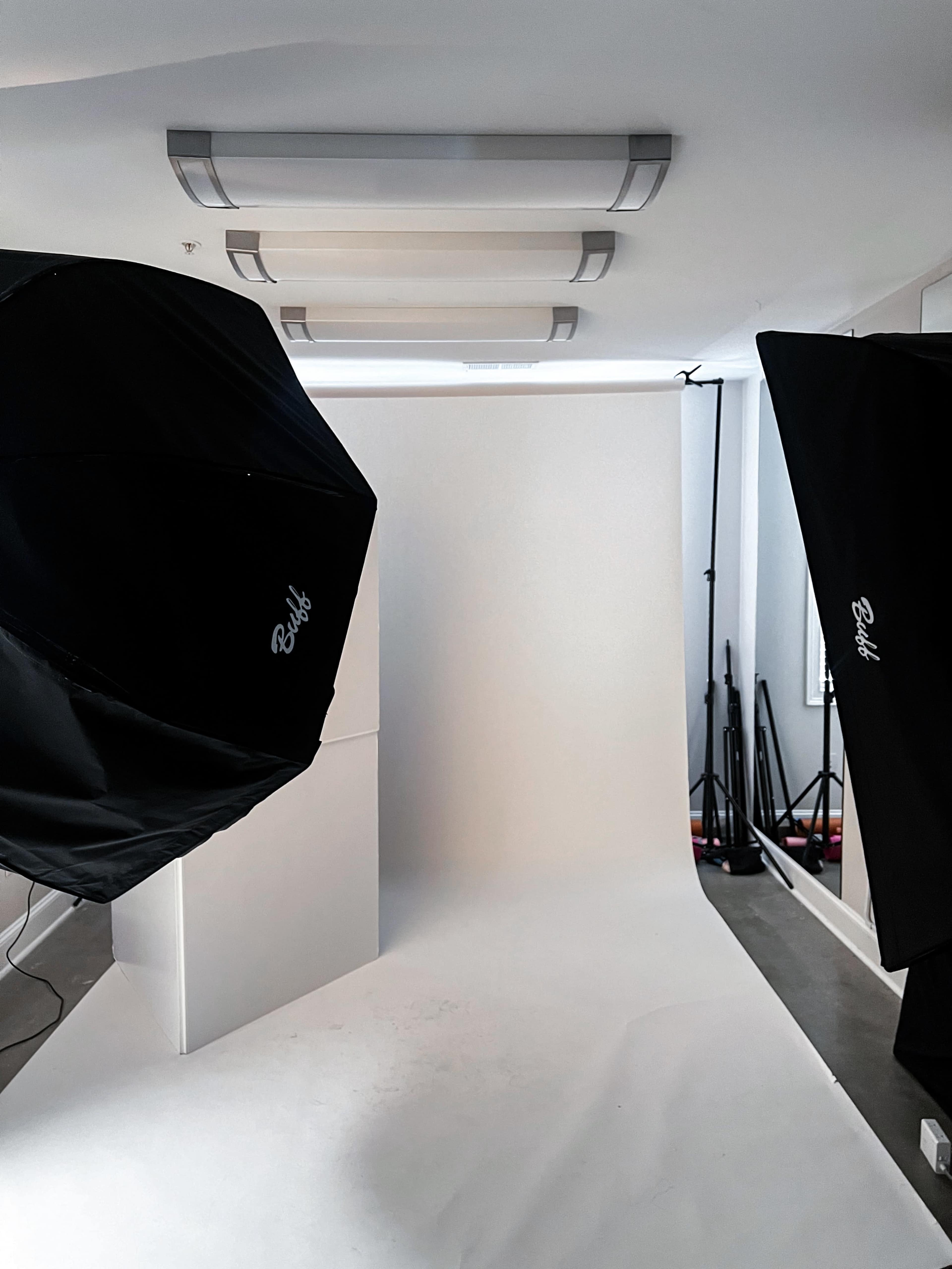 The image shows a photography studio setup with two black softbox lights positioned on either side of a plain white backdrop.