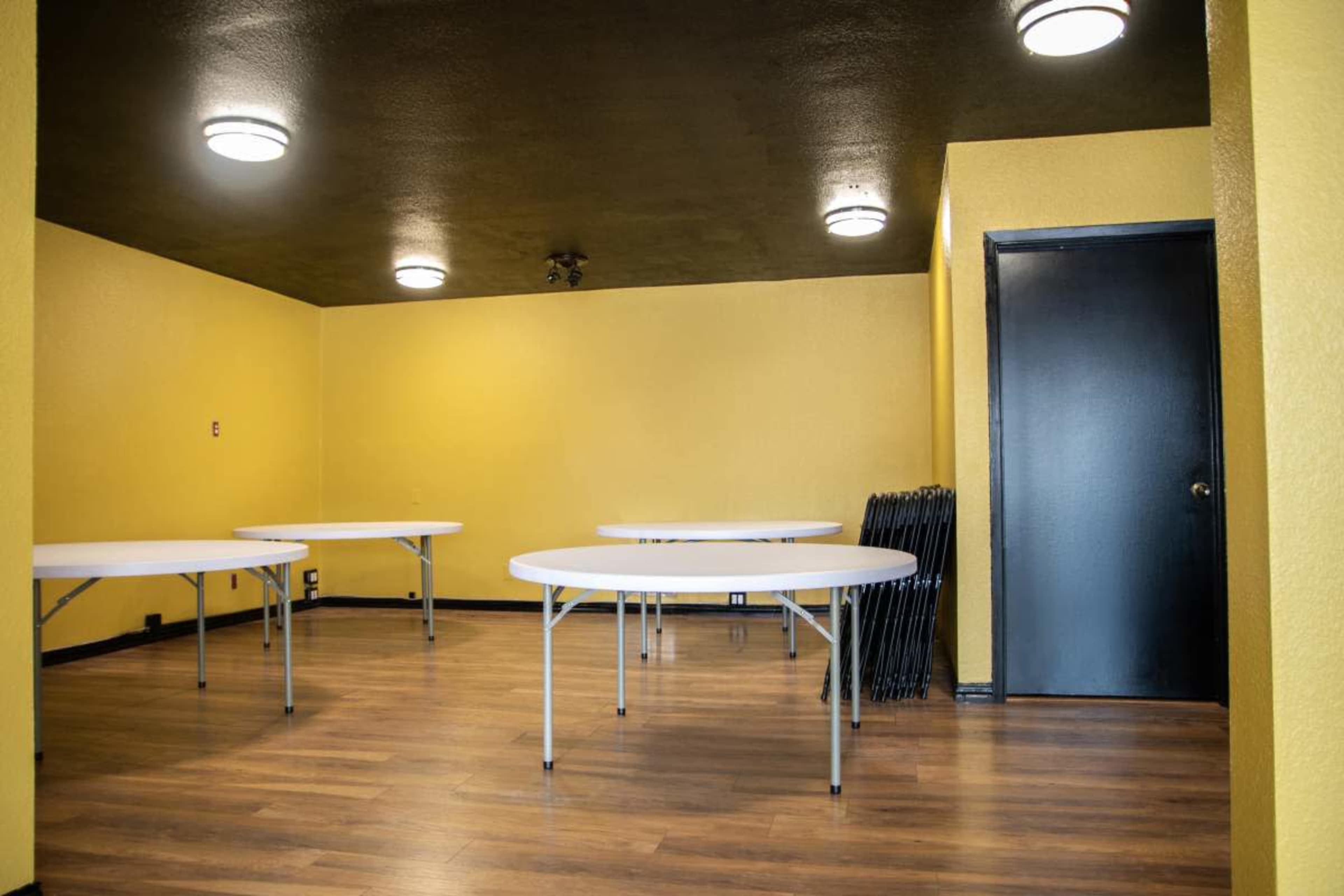 A brightly painted yellow room with several round tables set up and a black door on one wall.