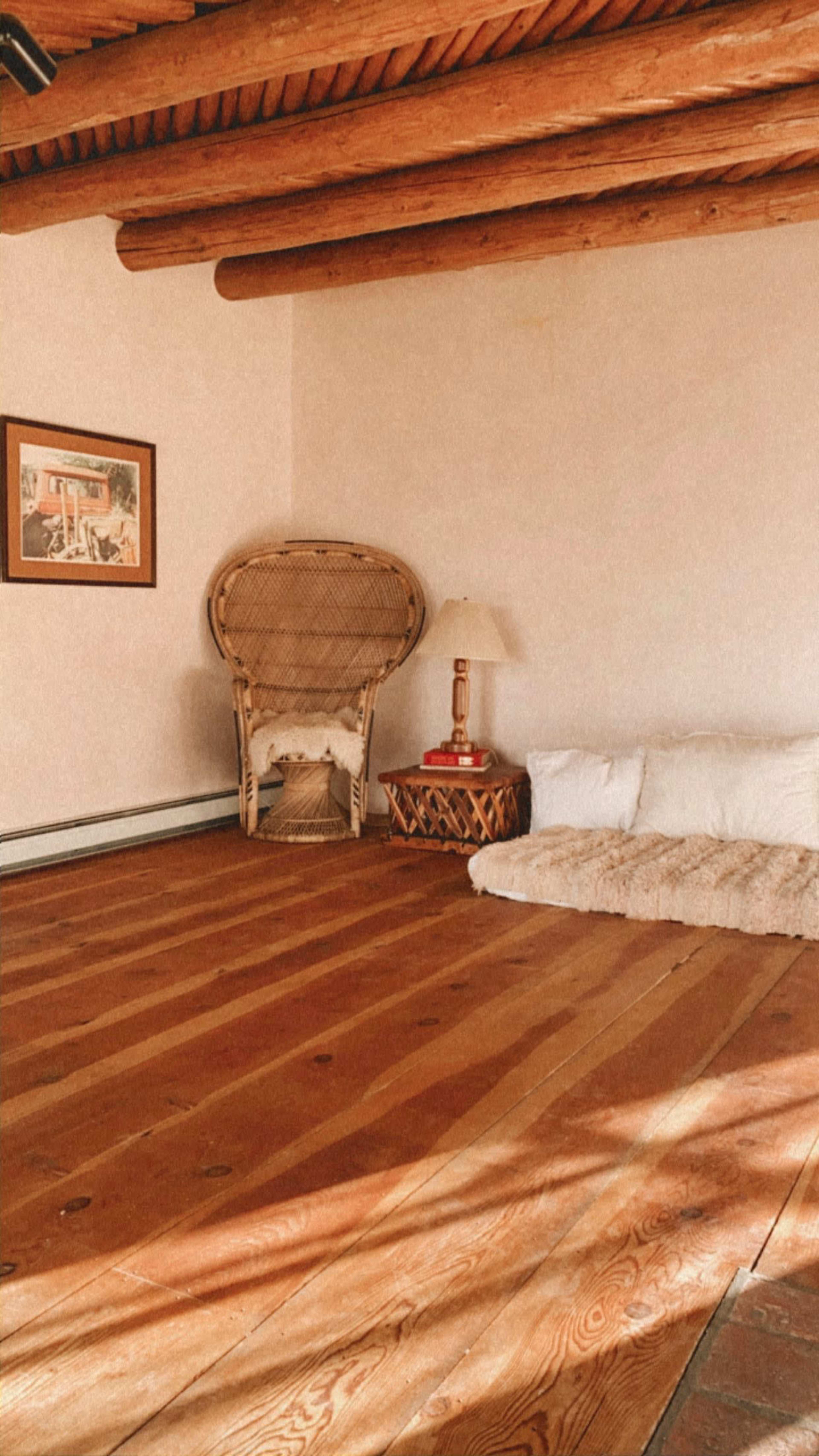 A spacious room with wooden floors, a large woven chair in the corner, and a low mattress with cushions on one side.
