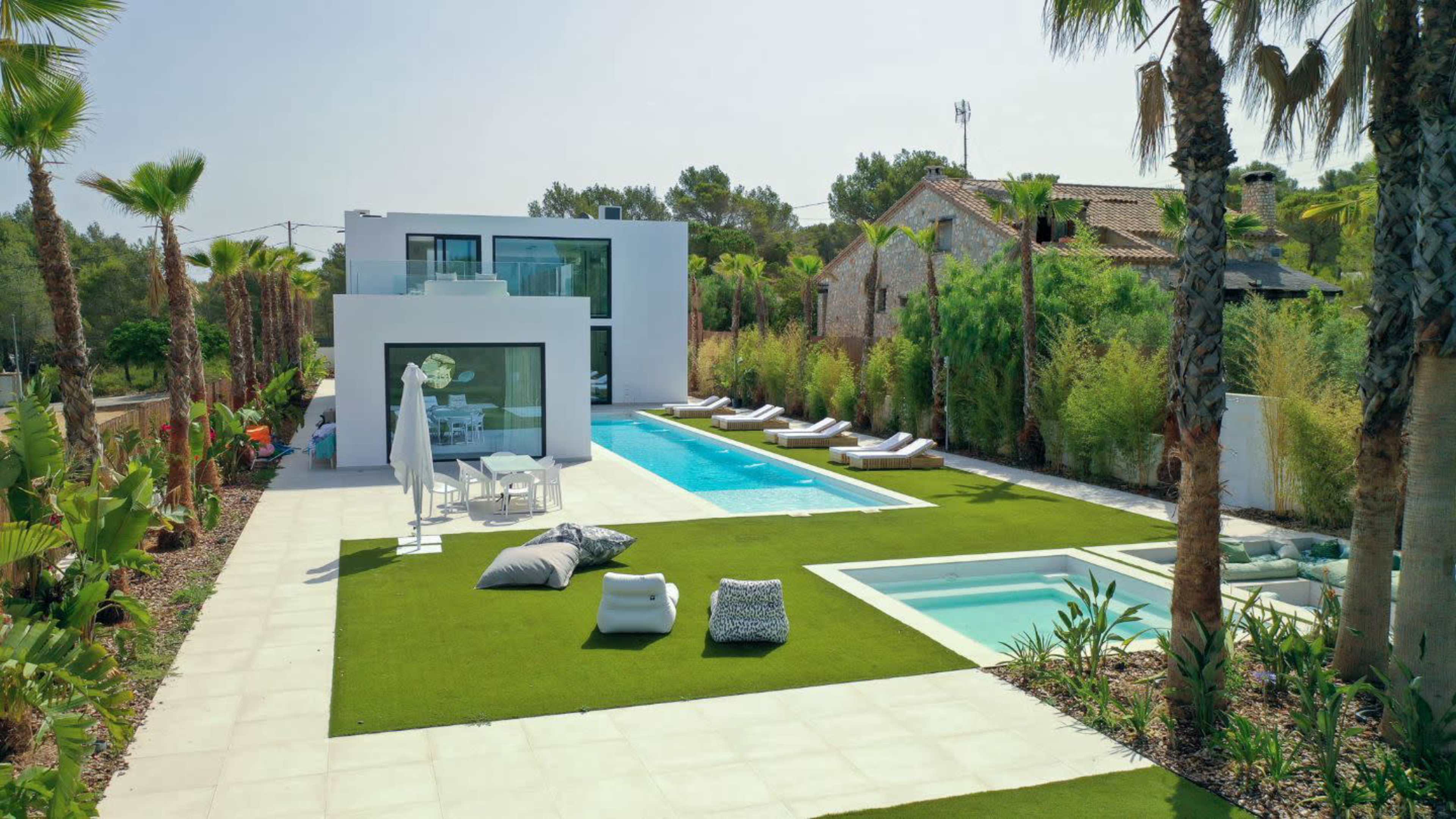 A modern villa with a swimming pool, surrounded by tropical landscaping and lounge chairs on a grassy area.