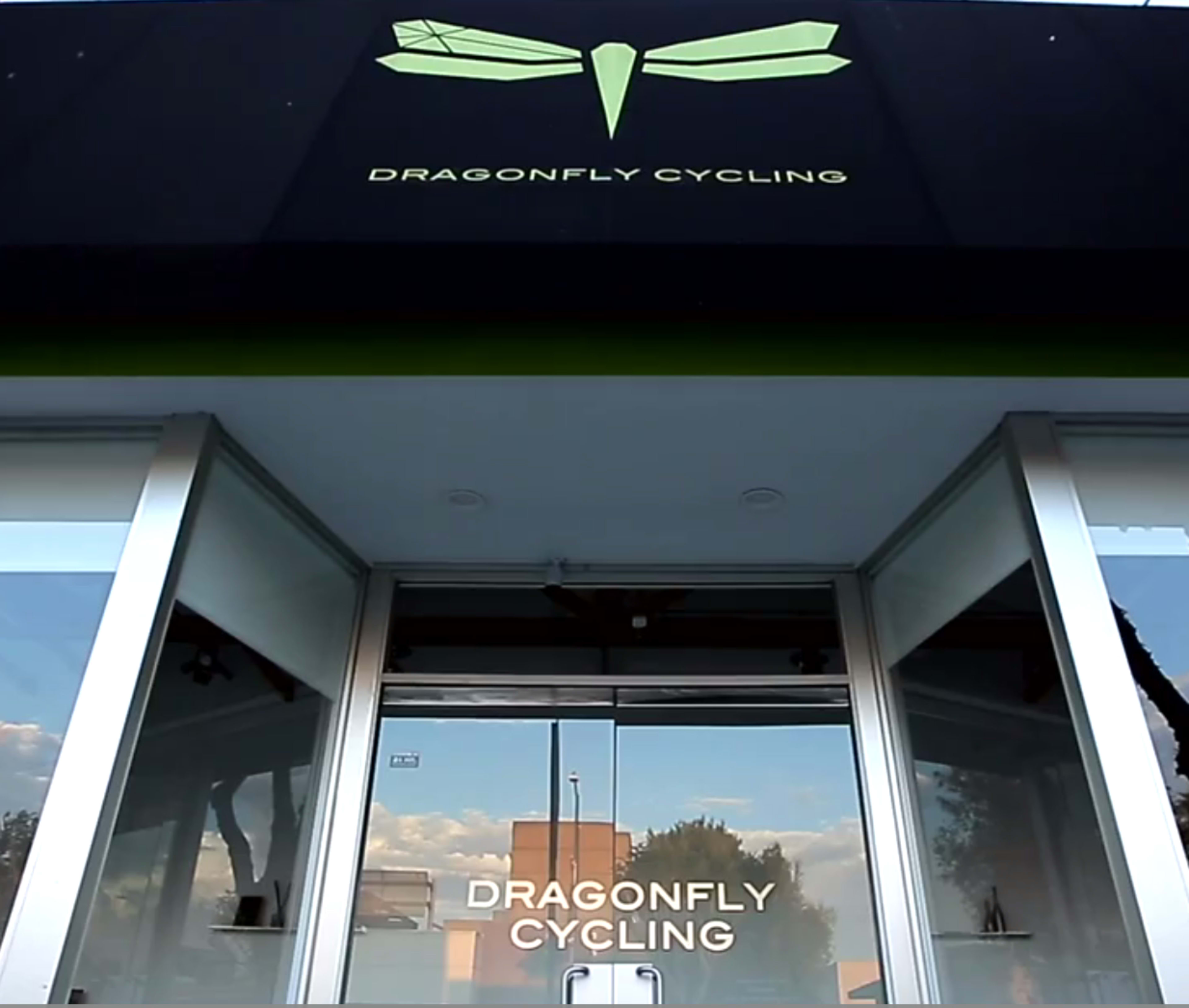 The image shows the entrance of a business named "Dragonfly Cycling," featuring a large sign with a dragonfly logo above the glass doors.