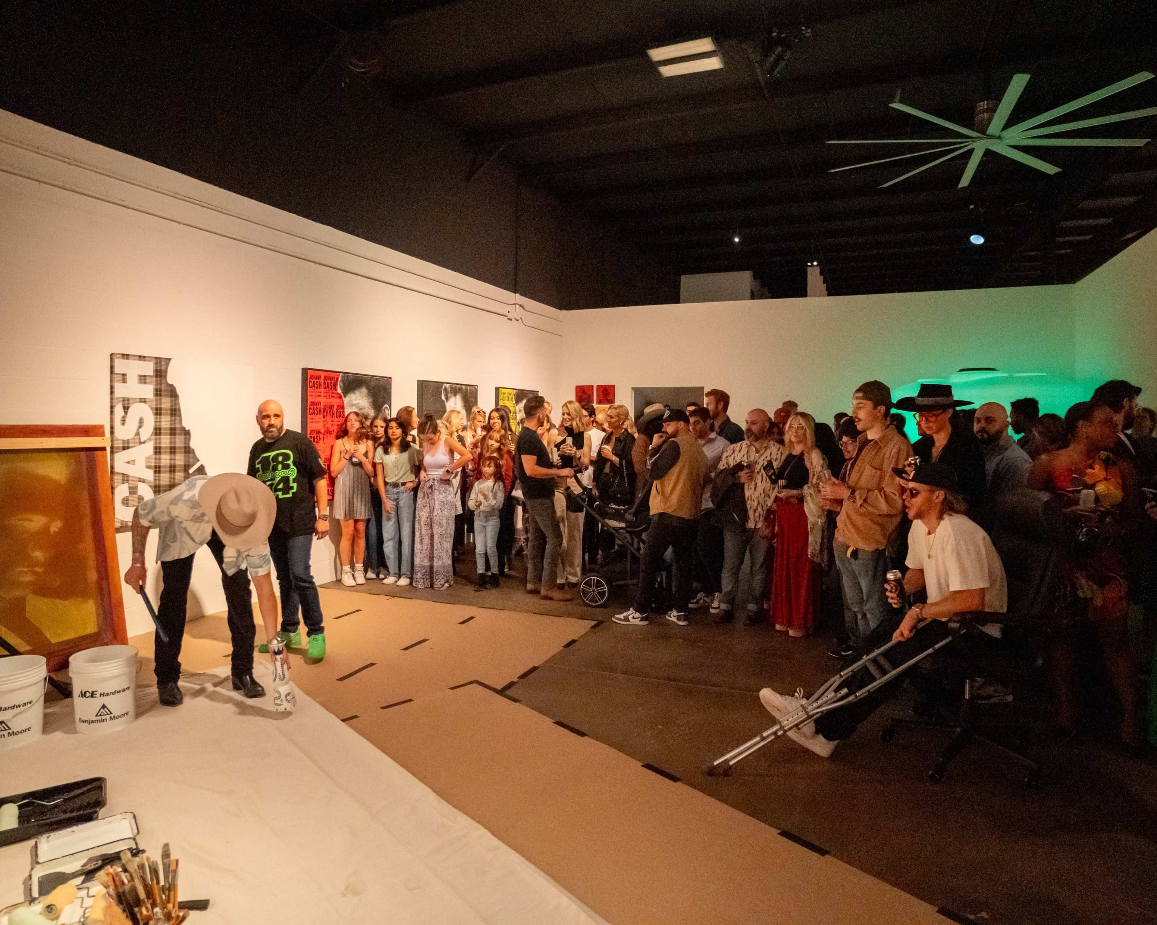 A large crowd of people watches an artist perform in an art gallery space.