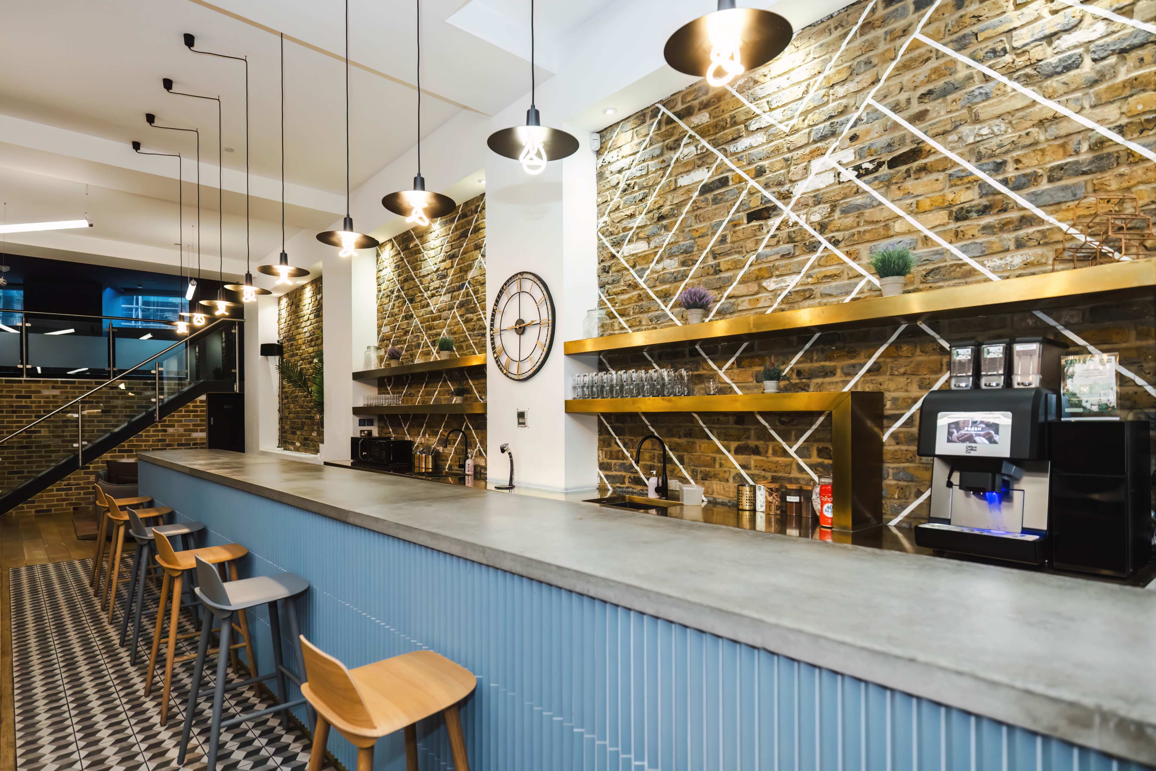 A modern café bar with a concrete countertop, wooden stools, and exposed brick walls featuring geometric designs.