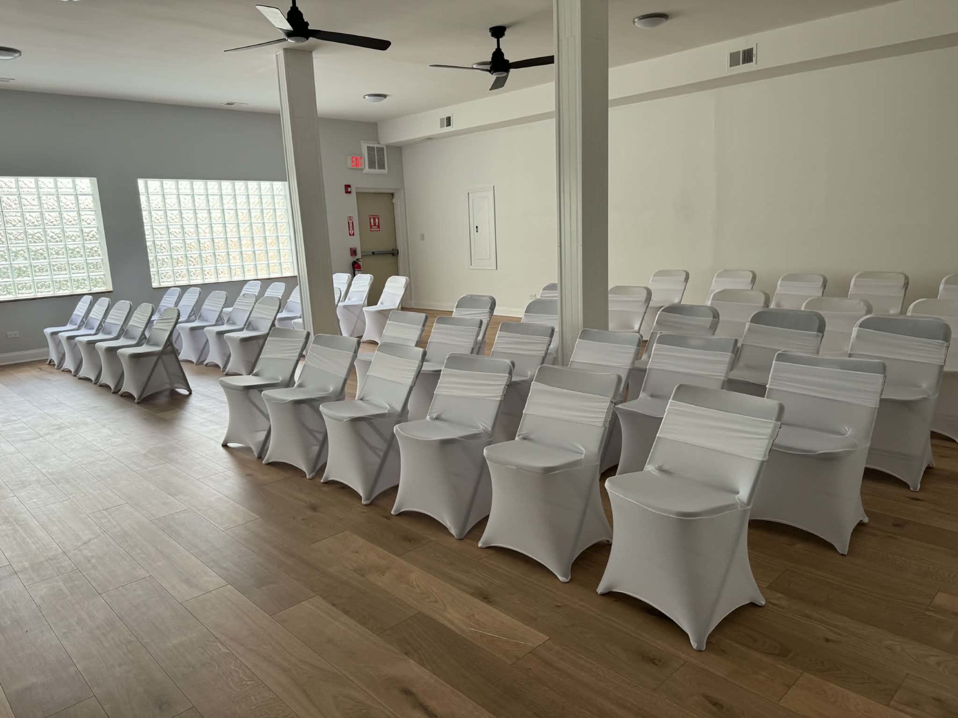 The image shows a well-lit room with a row of white chairs covered in fabric, arranged neatly on a wooden floor.