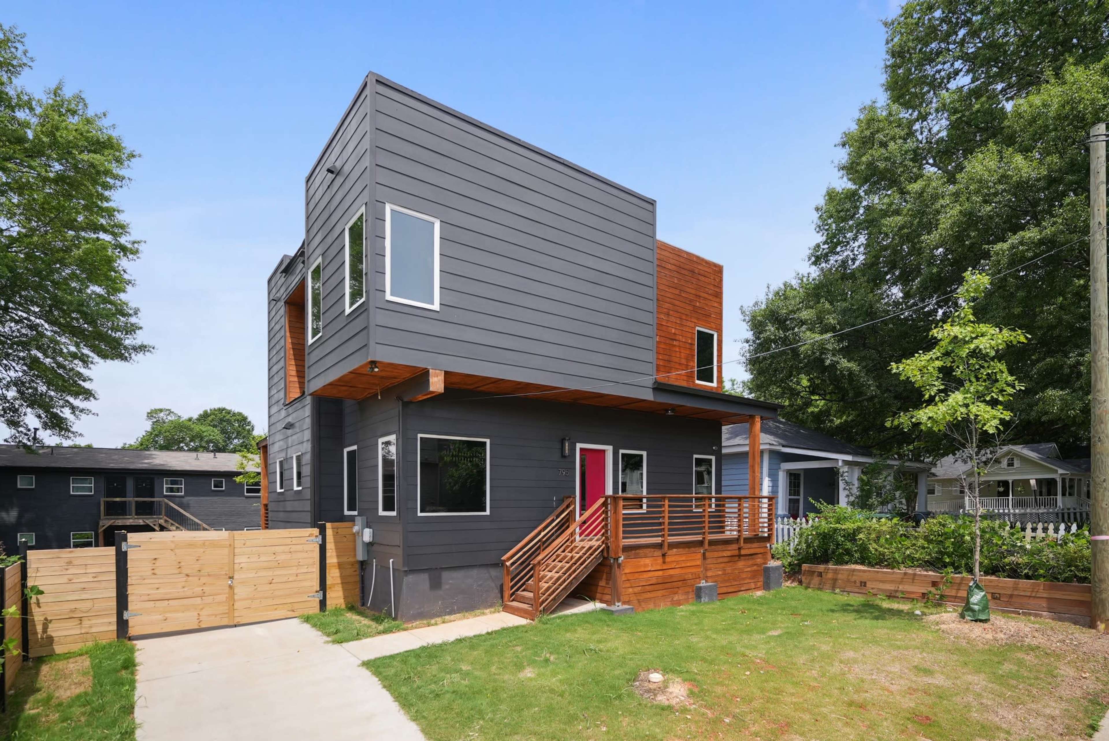 A modern two-story house features a combination of dark siding and warm wood accents, set within a landscaped yard.