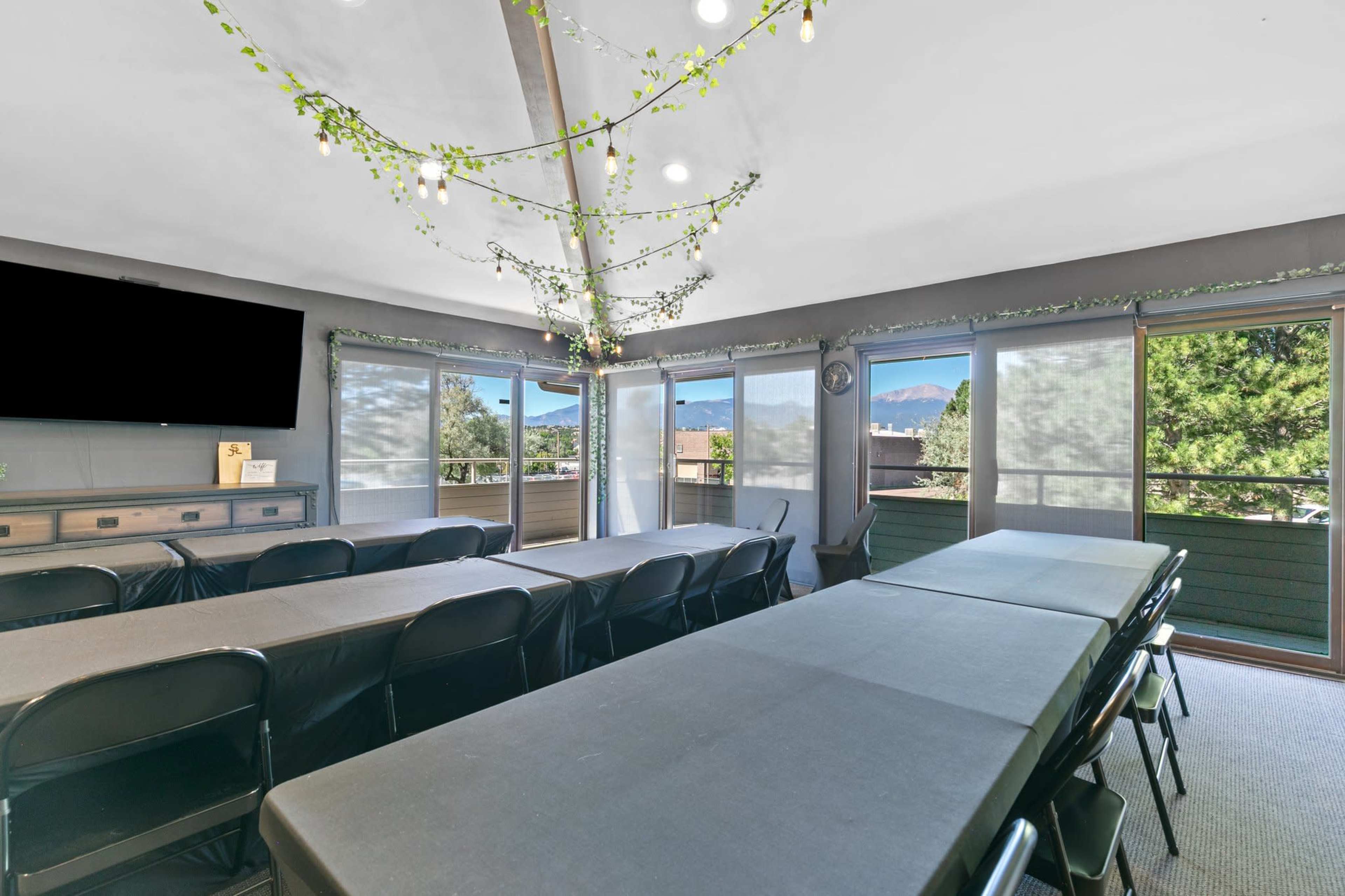 A modern conference room with long tables, black chairs, and a large window overlooking a mountainous landscape.