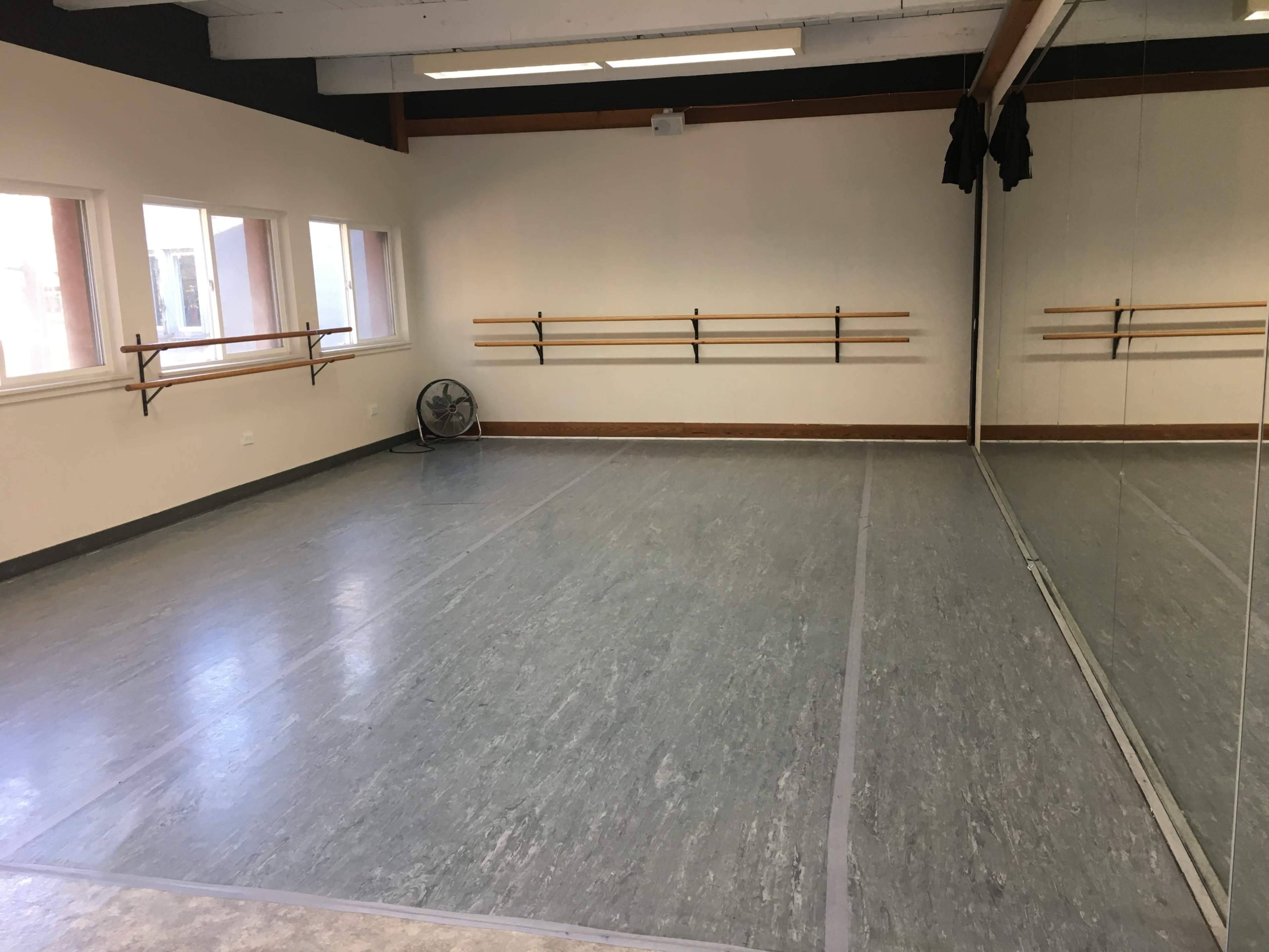 An empty dance studio with wooden ballet bars mounted on the wall and a large mirror along one side.
