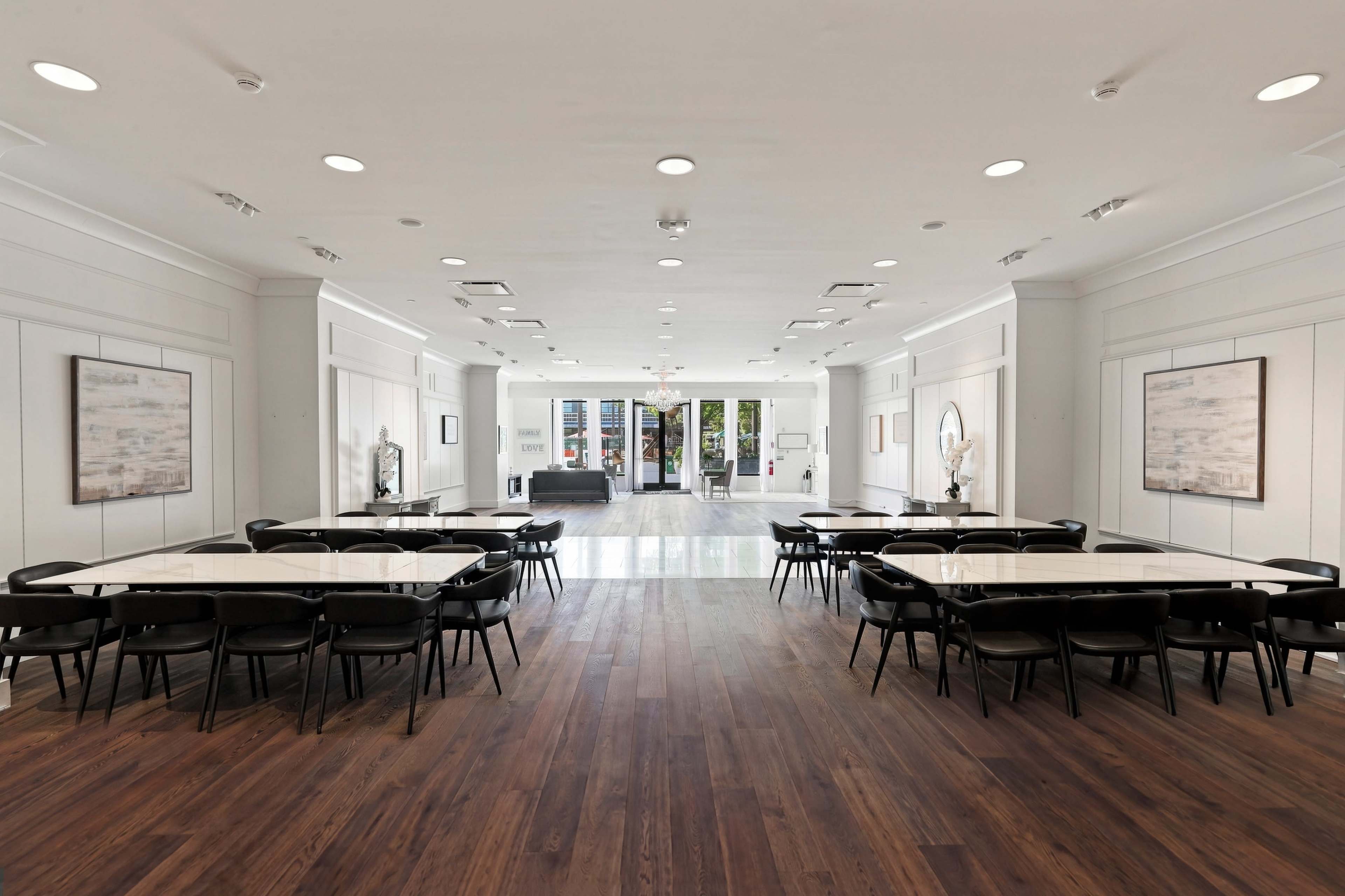 The image shows a spacious, modern event room with two long tables set for seating and large windows at the far end.