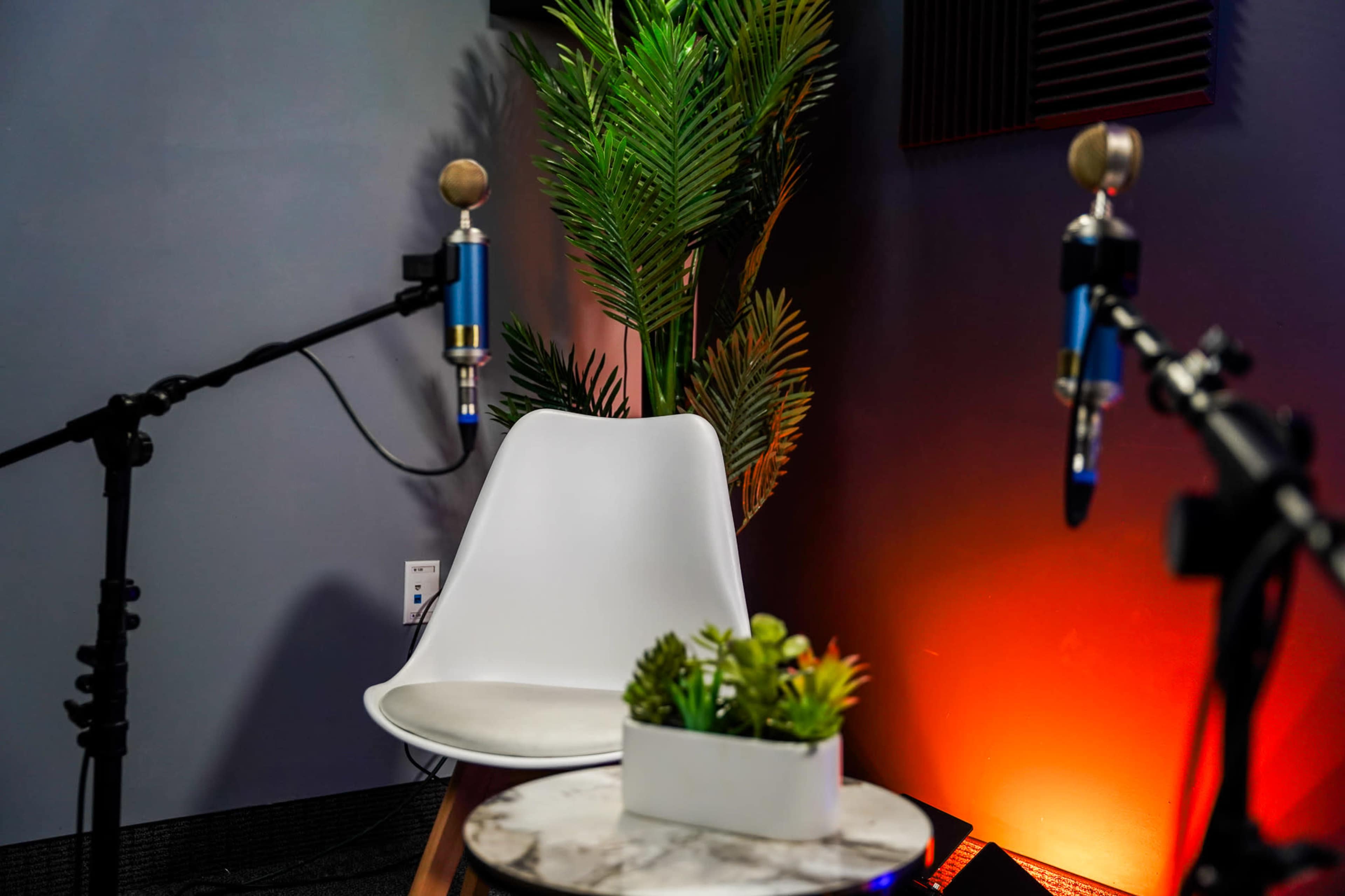 A white chair sits in a recording studio surrounded by microphones and a potted plant.