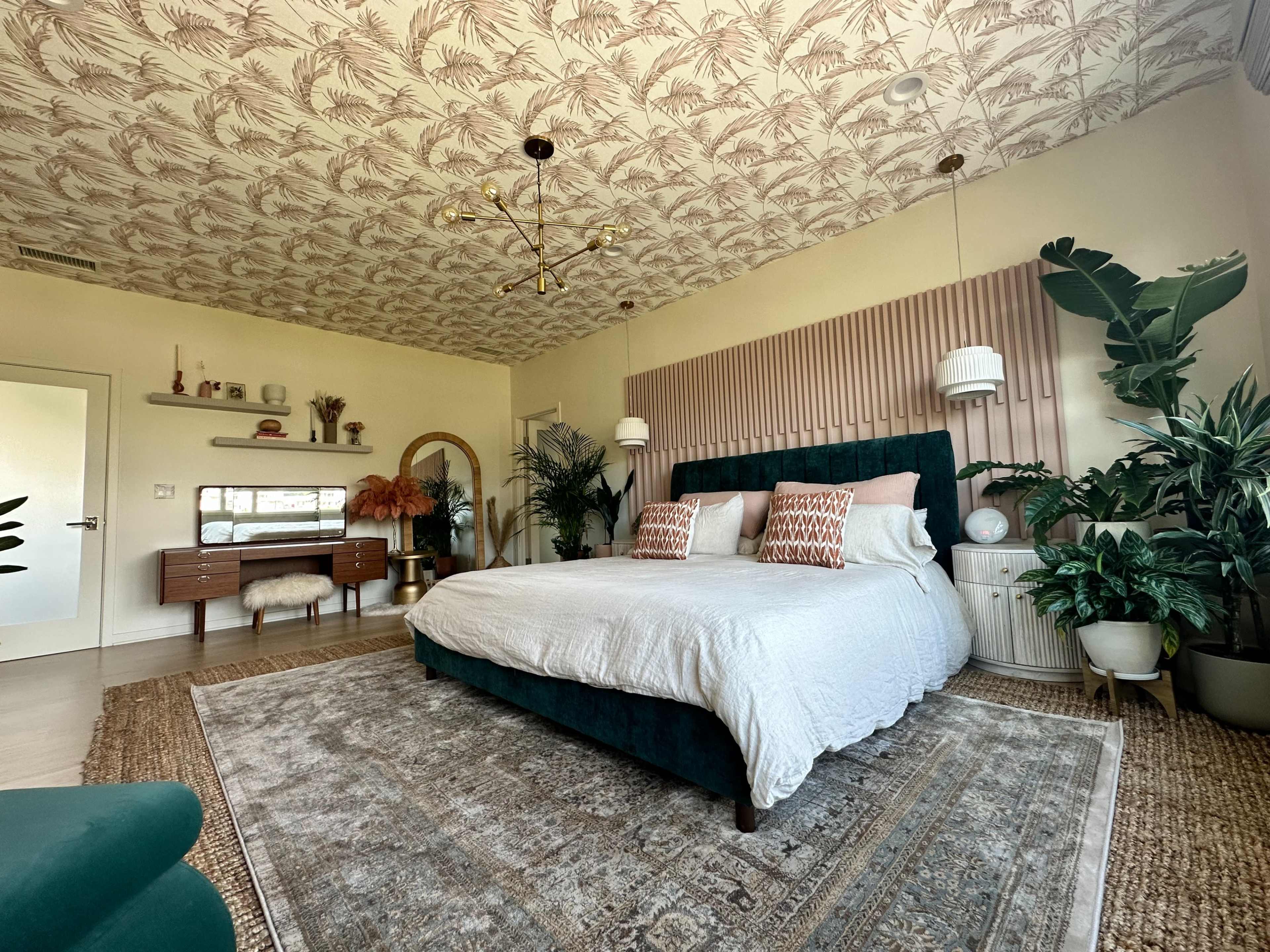 A neatly arranged bedroom features a large bed with a tufted headboard, surrounded by various indoor plants, a decorative ceiling, and a stylish dresser.