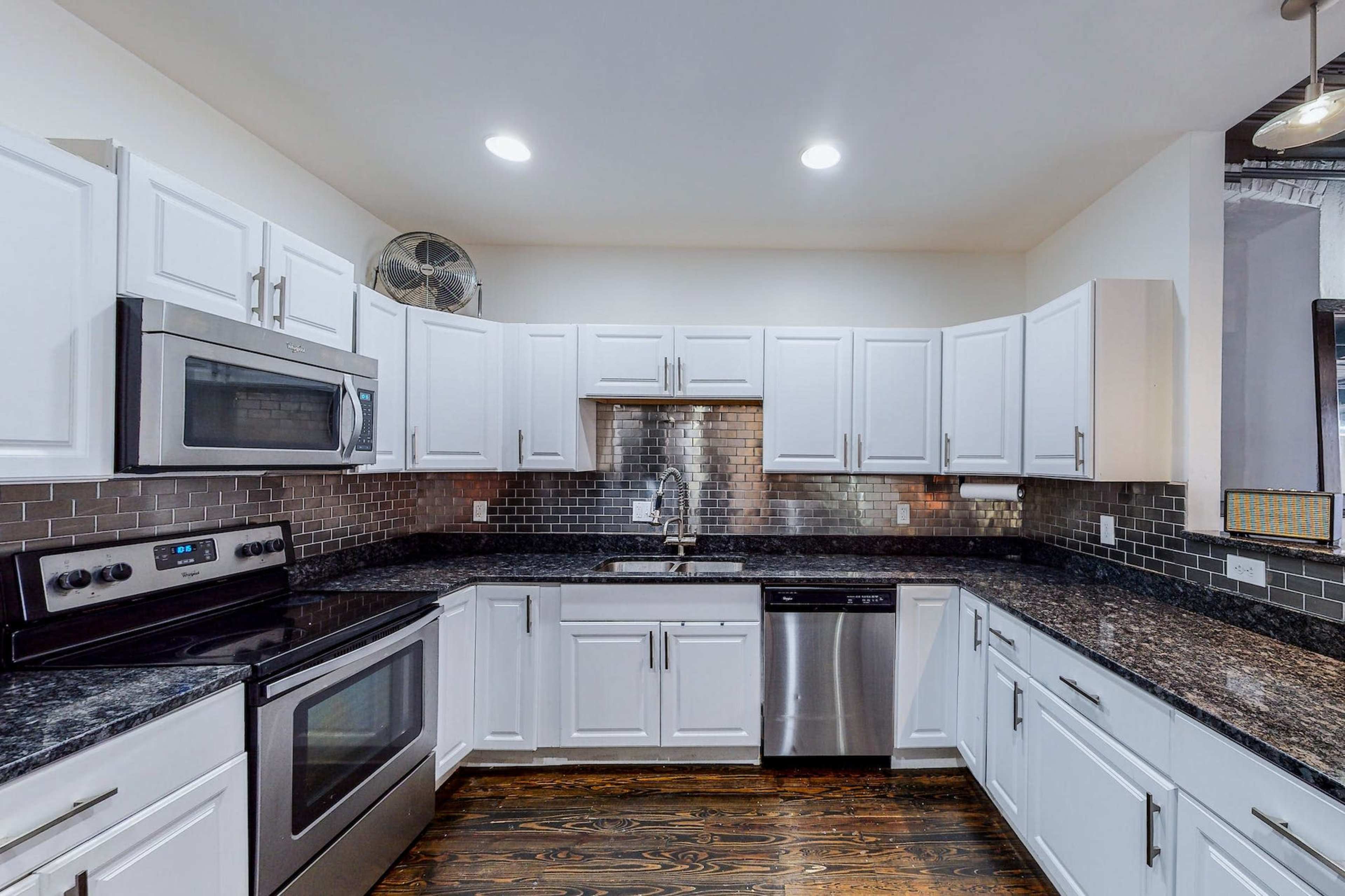 A modern kitchen with white cabinets, stainless steel appliances, and dark granite countertops.