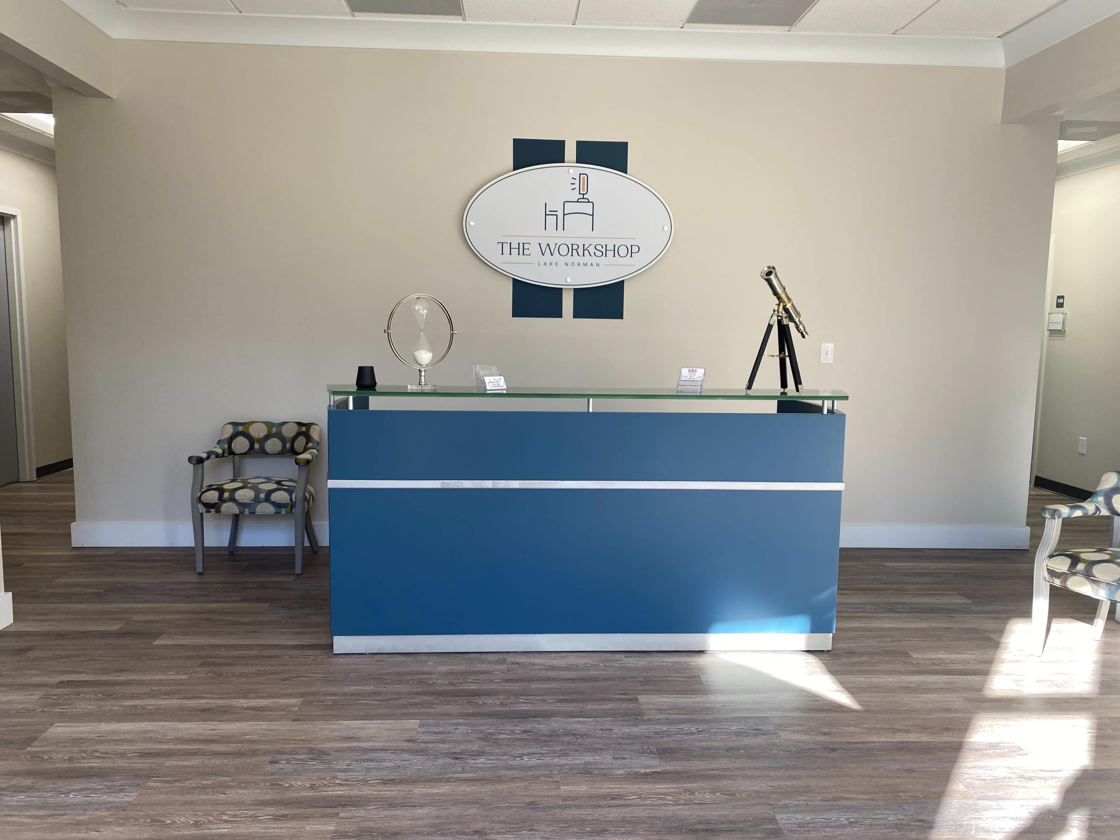 A modern reception area with a blue front desk, a decorative mirror, and a telescope displayed on the counter, along with a patterned chair in the corner.