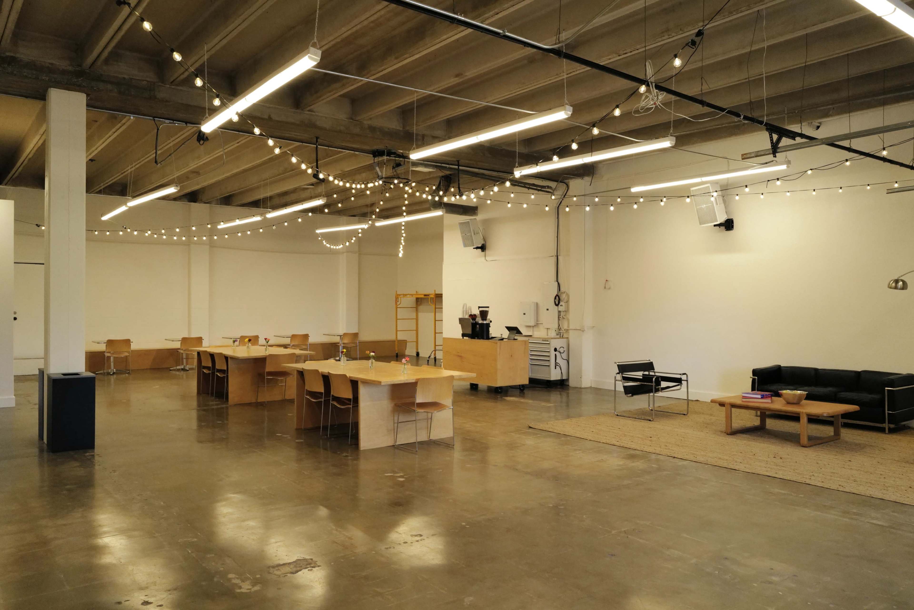 The image shows a spacious, modern interior with wooden furniture, string lights overhead, and a seating area featuring a black couch and a coffee table.
