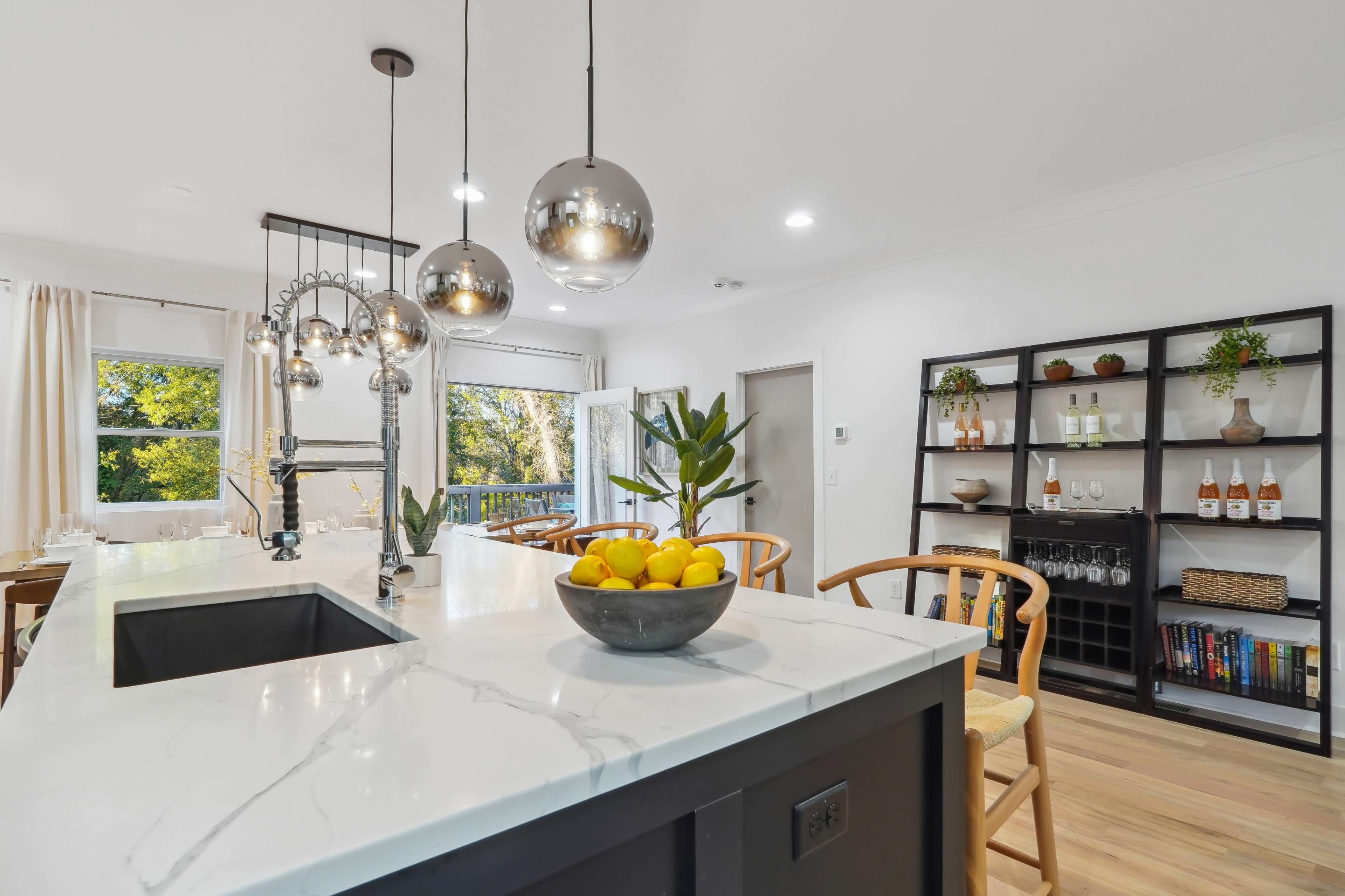 A modern kitchen with a large island featuring a bowl of lemons, pendant lights overhead, and a dining area in the background.