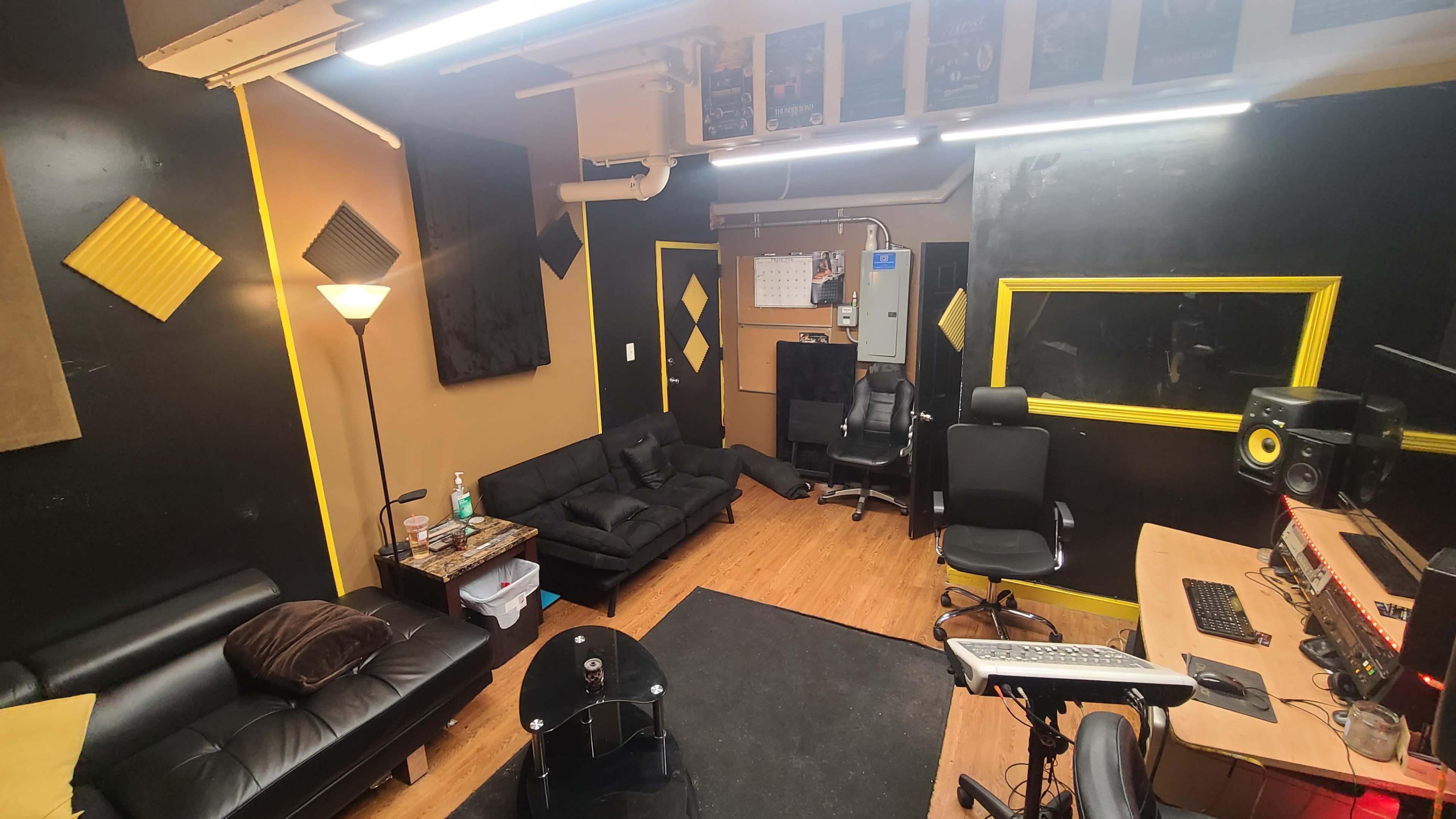 A music studio with black and yellow walls, featuring seating areas, a control desk, and soundproof panels.