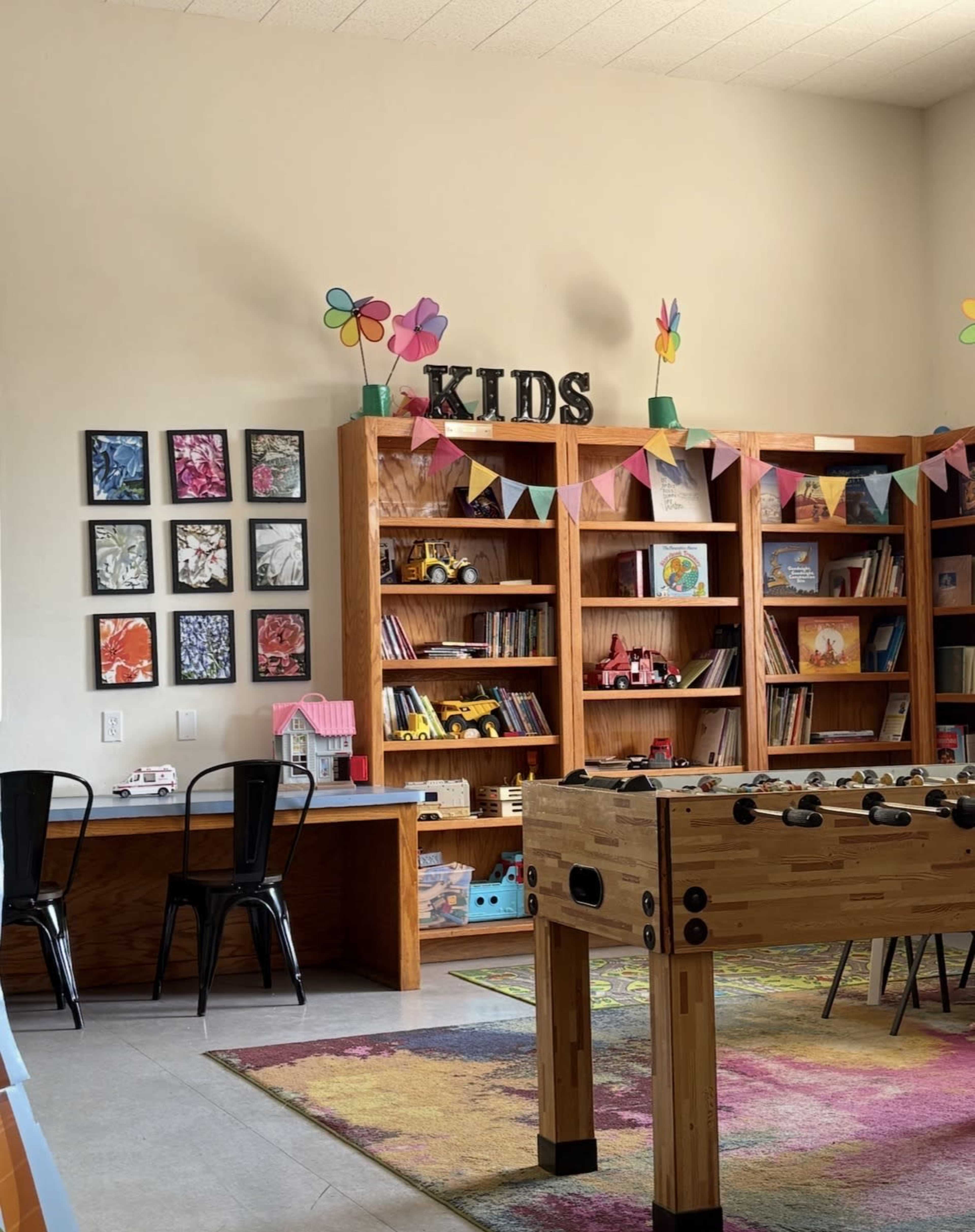 The image depicts a children's reading room featuring a bookshelf filled with books and toys, a foosball table, and colorful decorations.