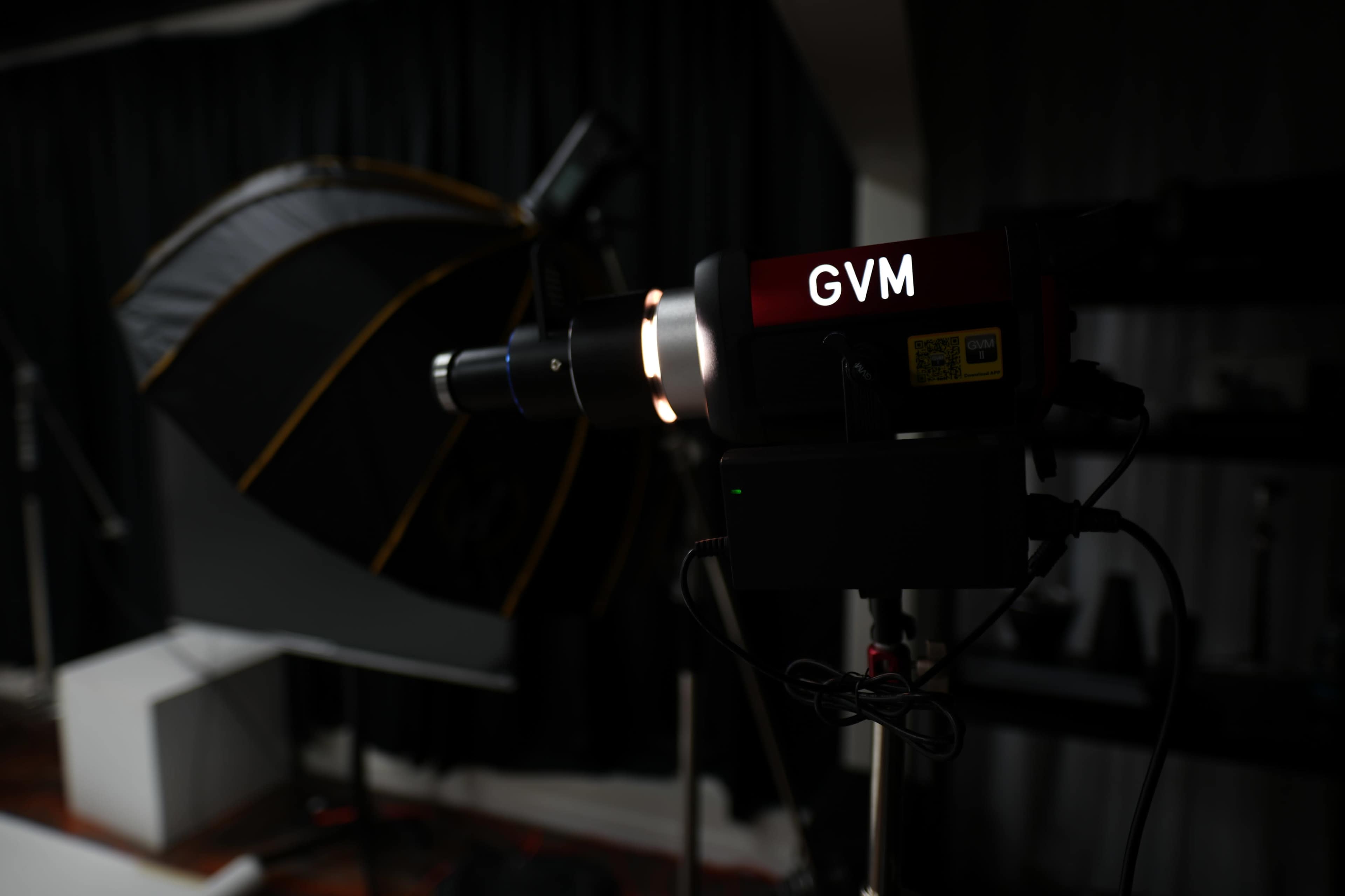A GVM light fixture is positioned in front of a photography umbrella reflector in a studio setting.