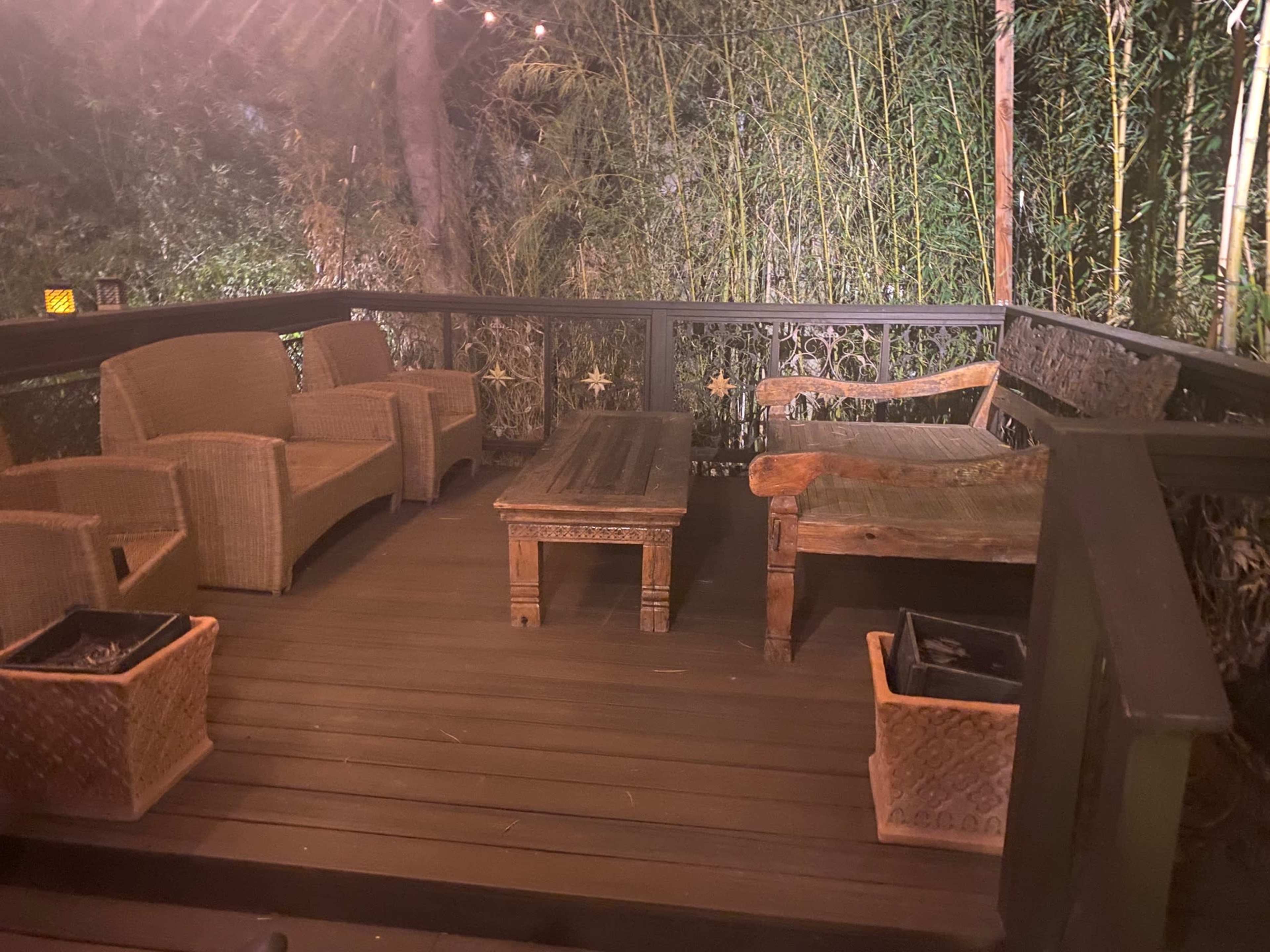 The image shows a wooden deck area with a table and several wicker chairs surrounded by bamboo plants.