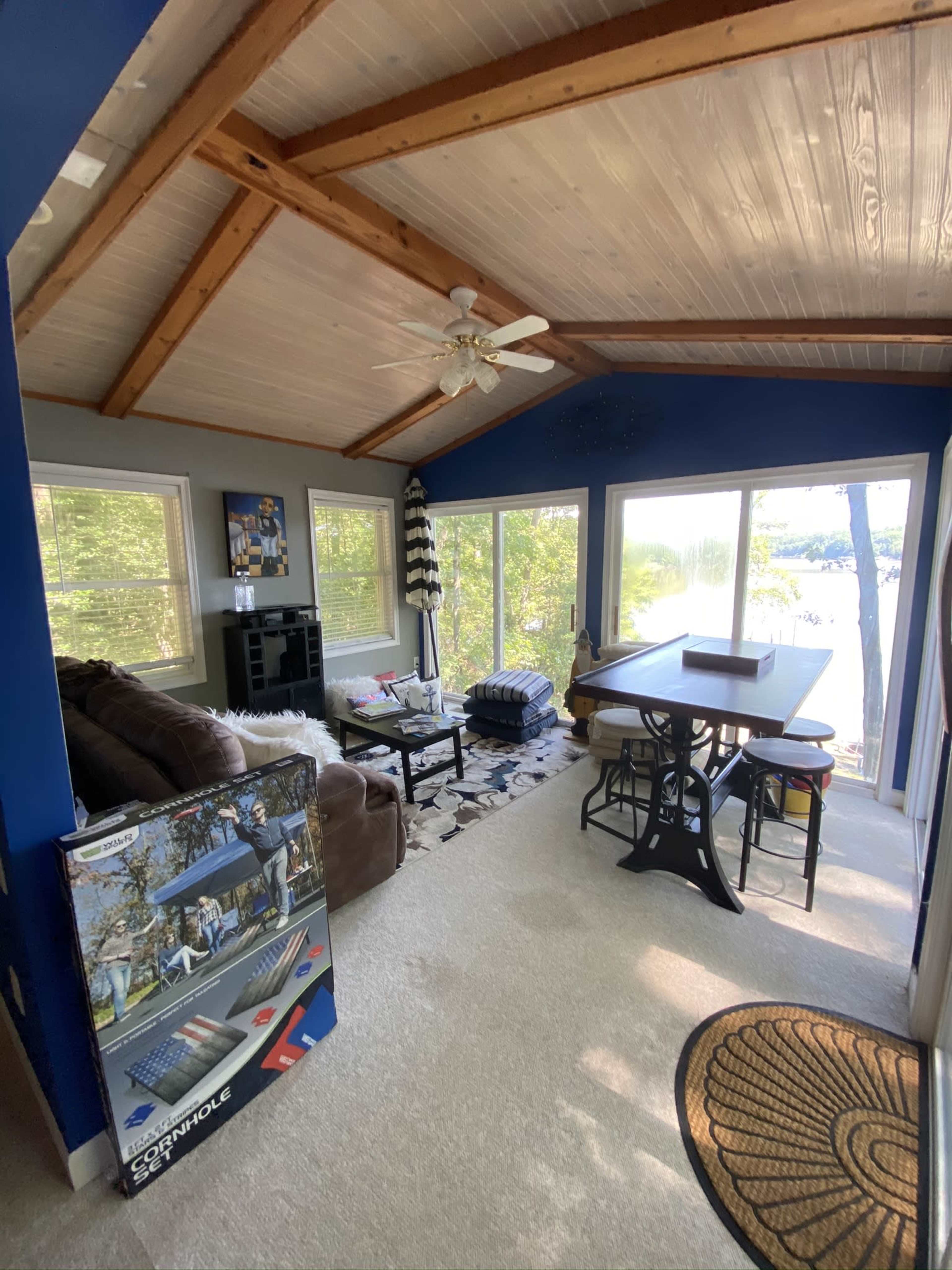 A cozy room with a vaulted ceiling features large windows overlooking a lake, furnished with a sofa, table, and decorative elements.