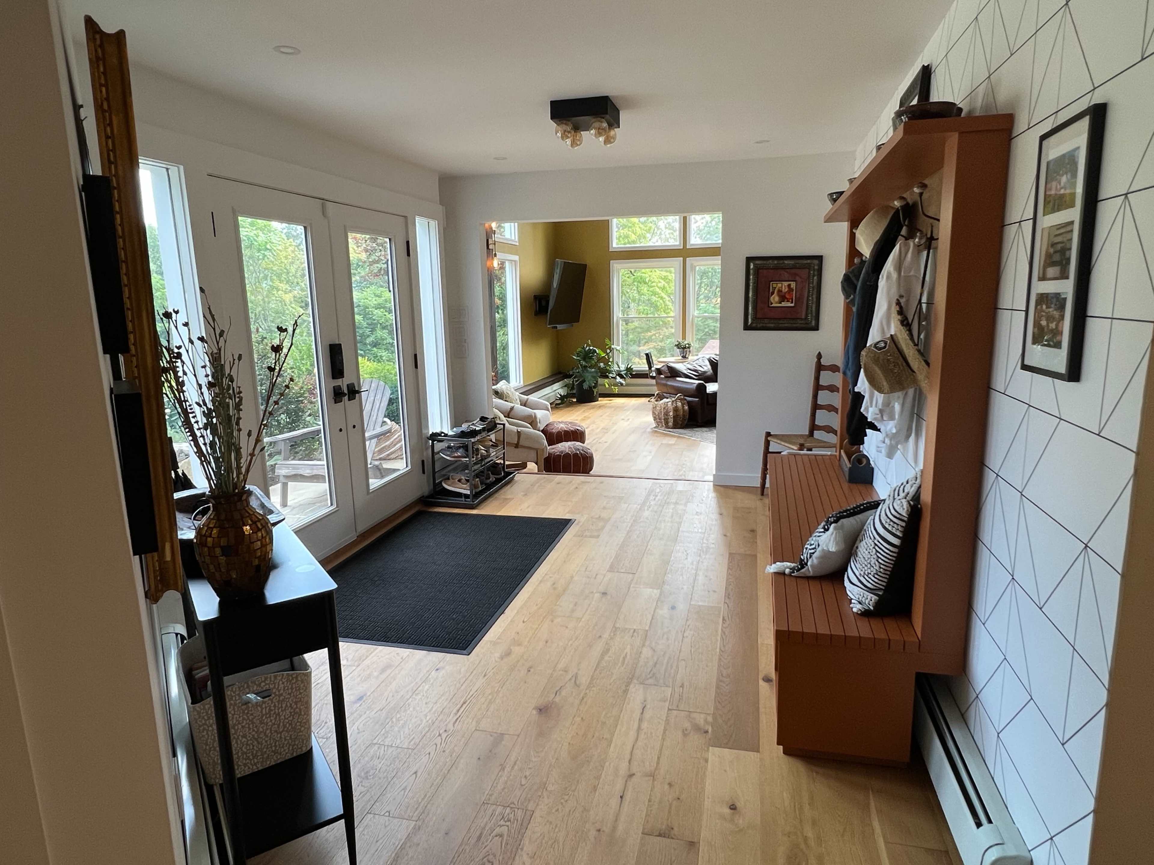 A spacious entryway with a view of a living area, featuring large windows and wooden flooring.