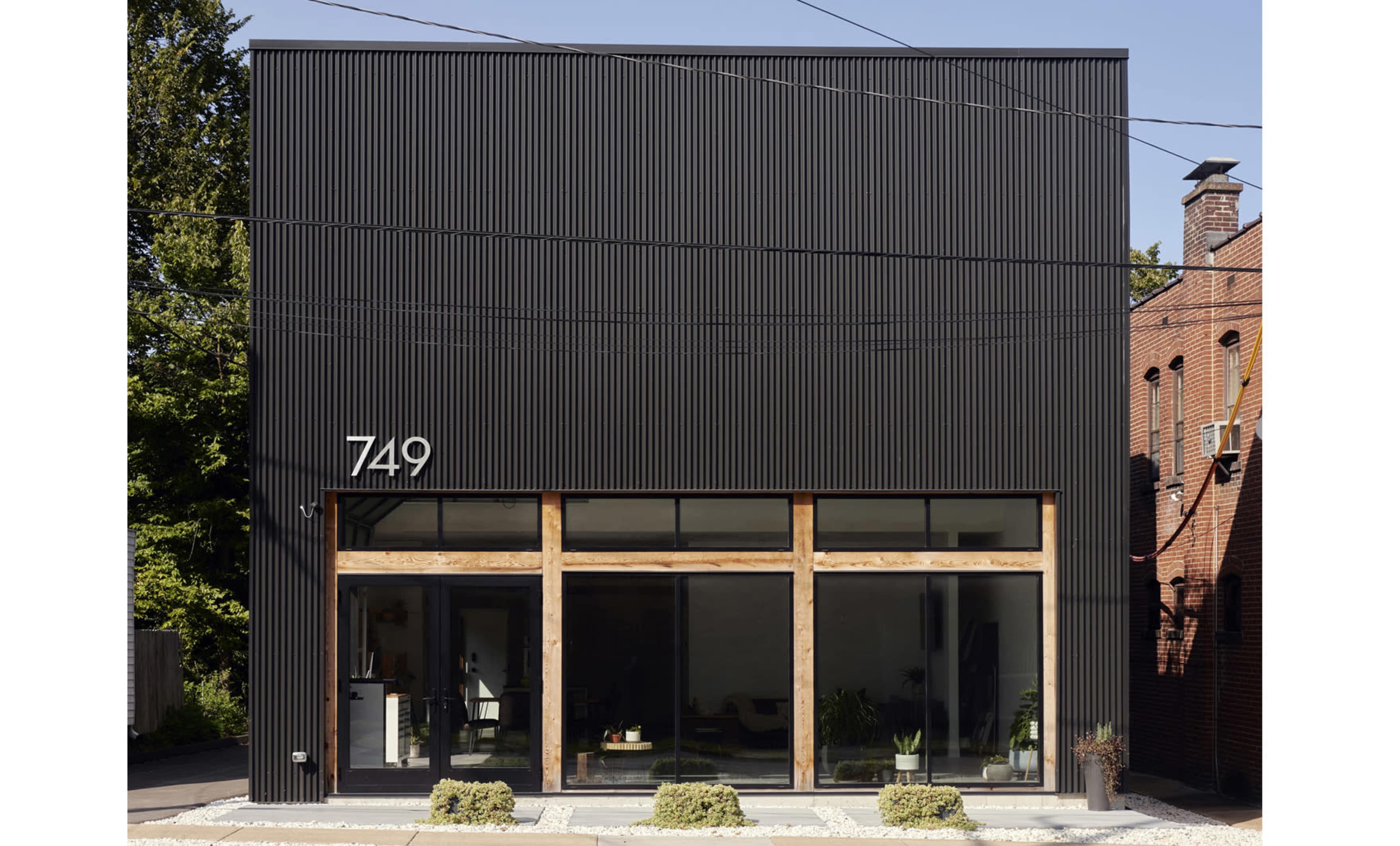 The image shows a modern black-cladded building with large front windows and the number 749 displayed prominently above the entrance.