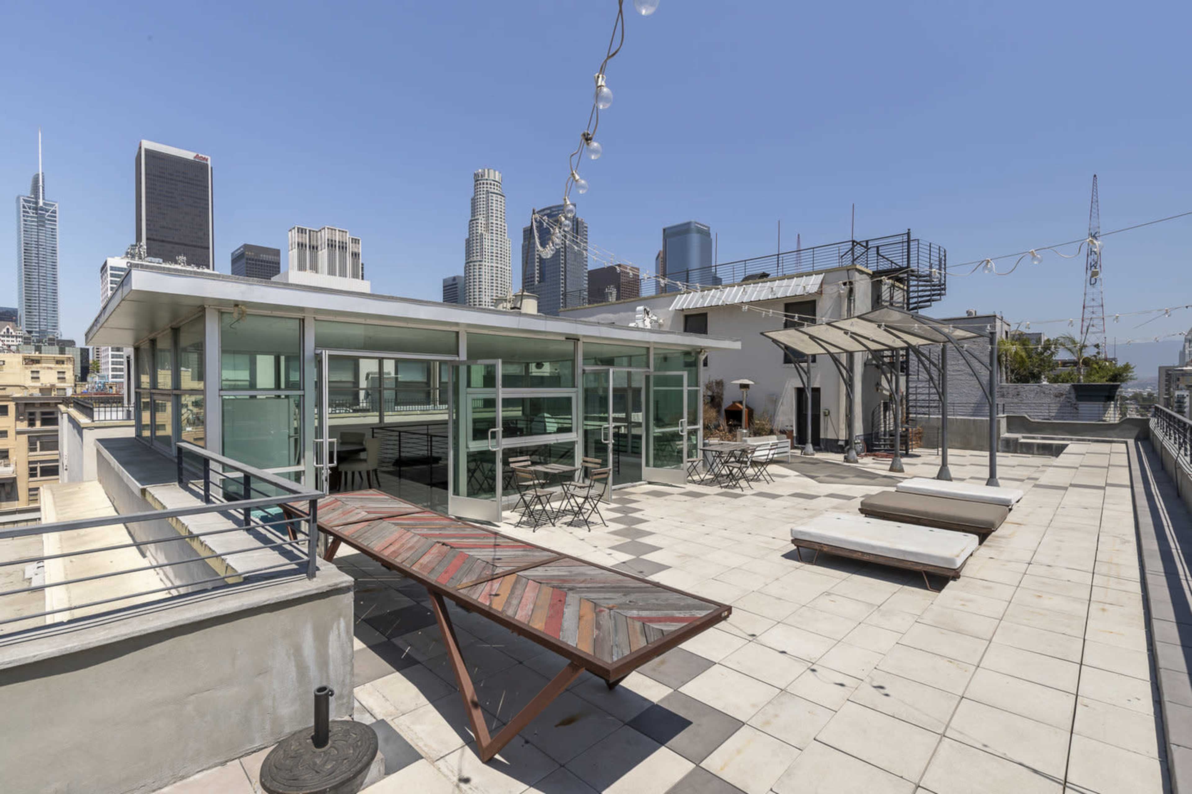 The rooftop features a spacious area with glass walls, tables, and lounge chairs, overlooking the downtown skyline.