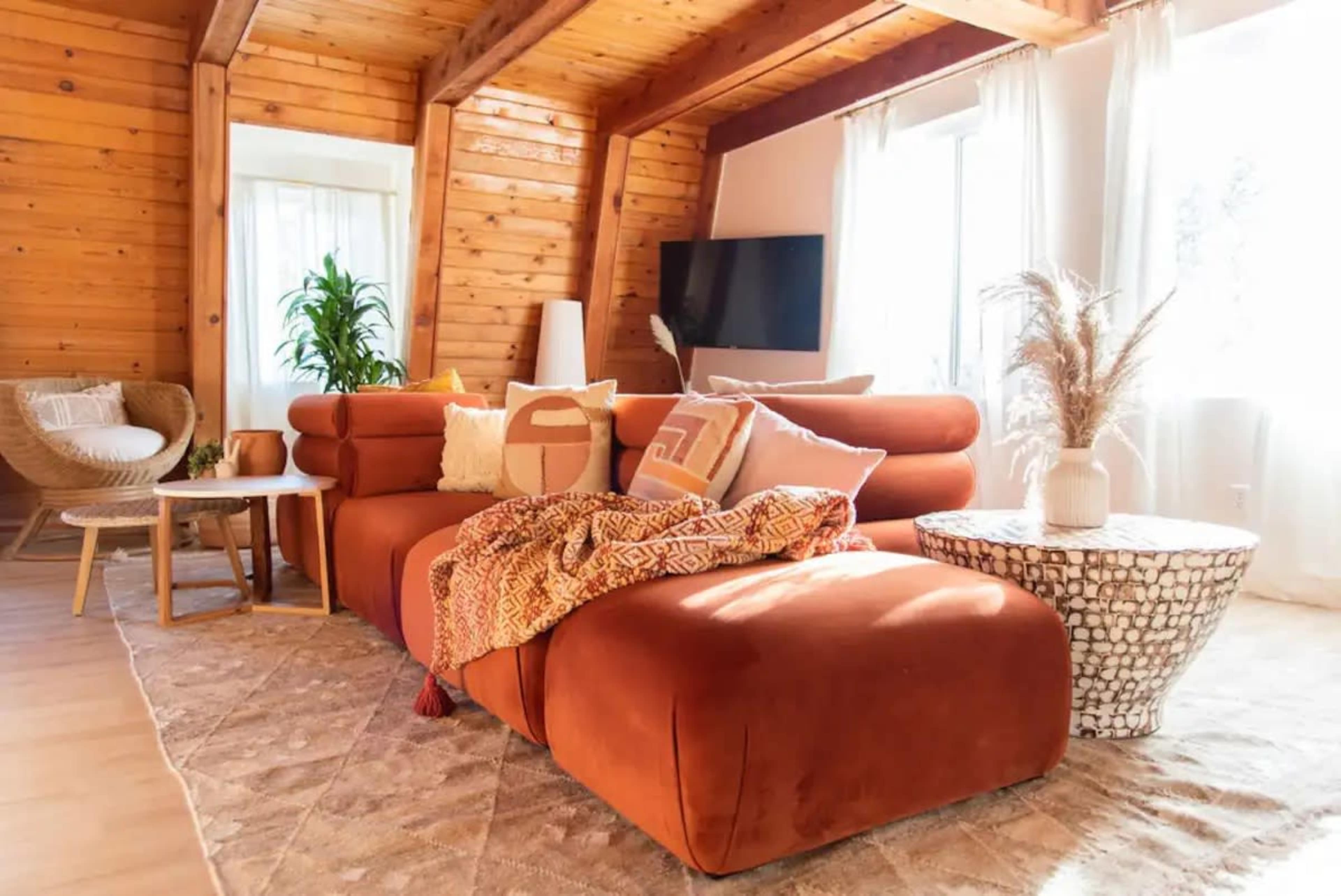 A modern living room with a large orange sectional sofa, a round coffee table, and large windows letting in natural light.
