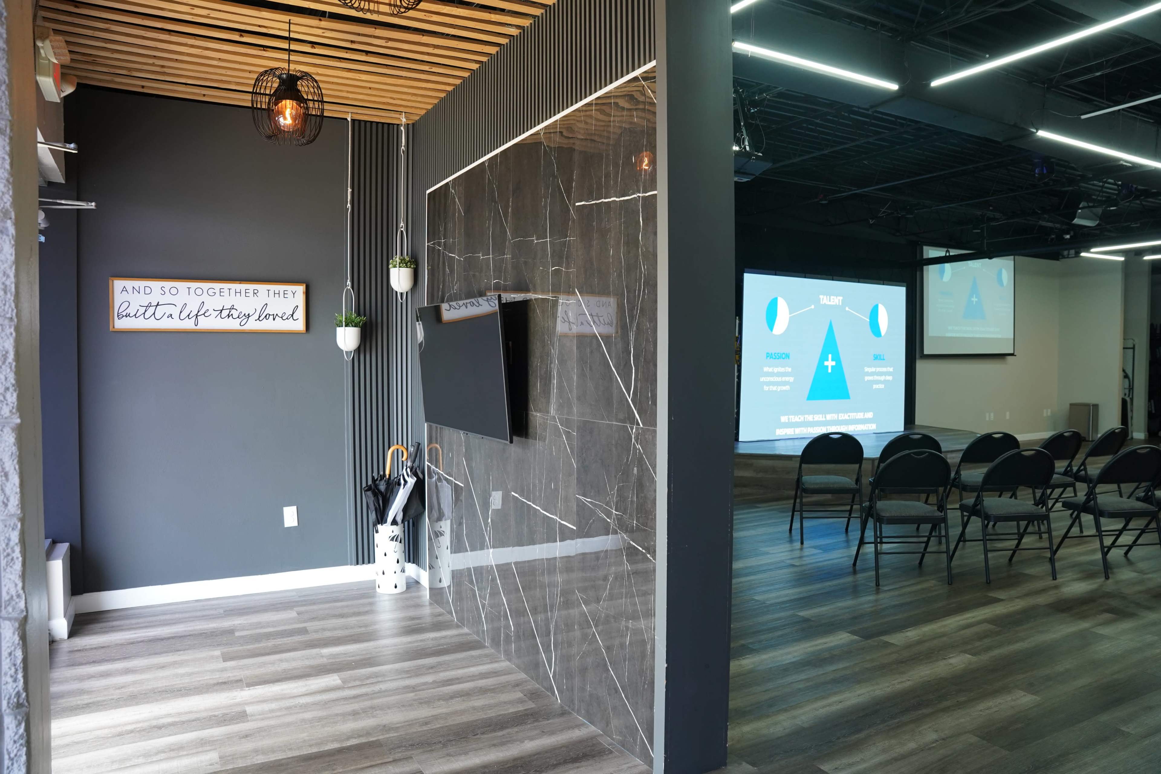 The image shows a modern interior space with a wall-mounted television and a projection screen, surrounded by seating chairs in a well-lit room.