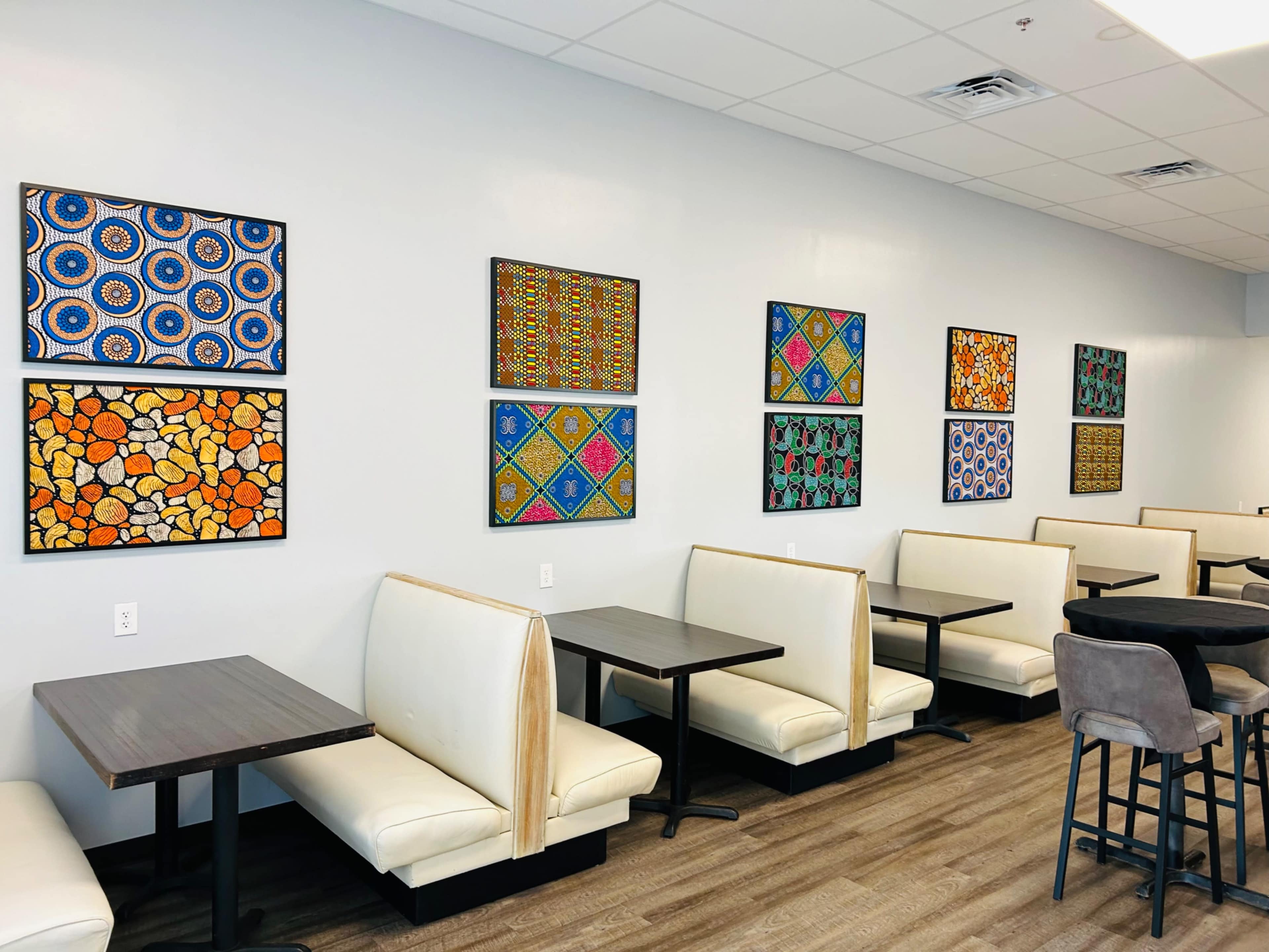 A light-colored restaurant interior with white booths and tables, featuring vibrant patterned artwork on the walls.