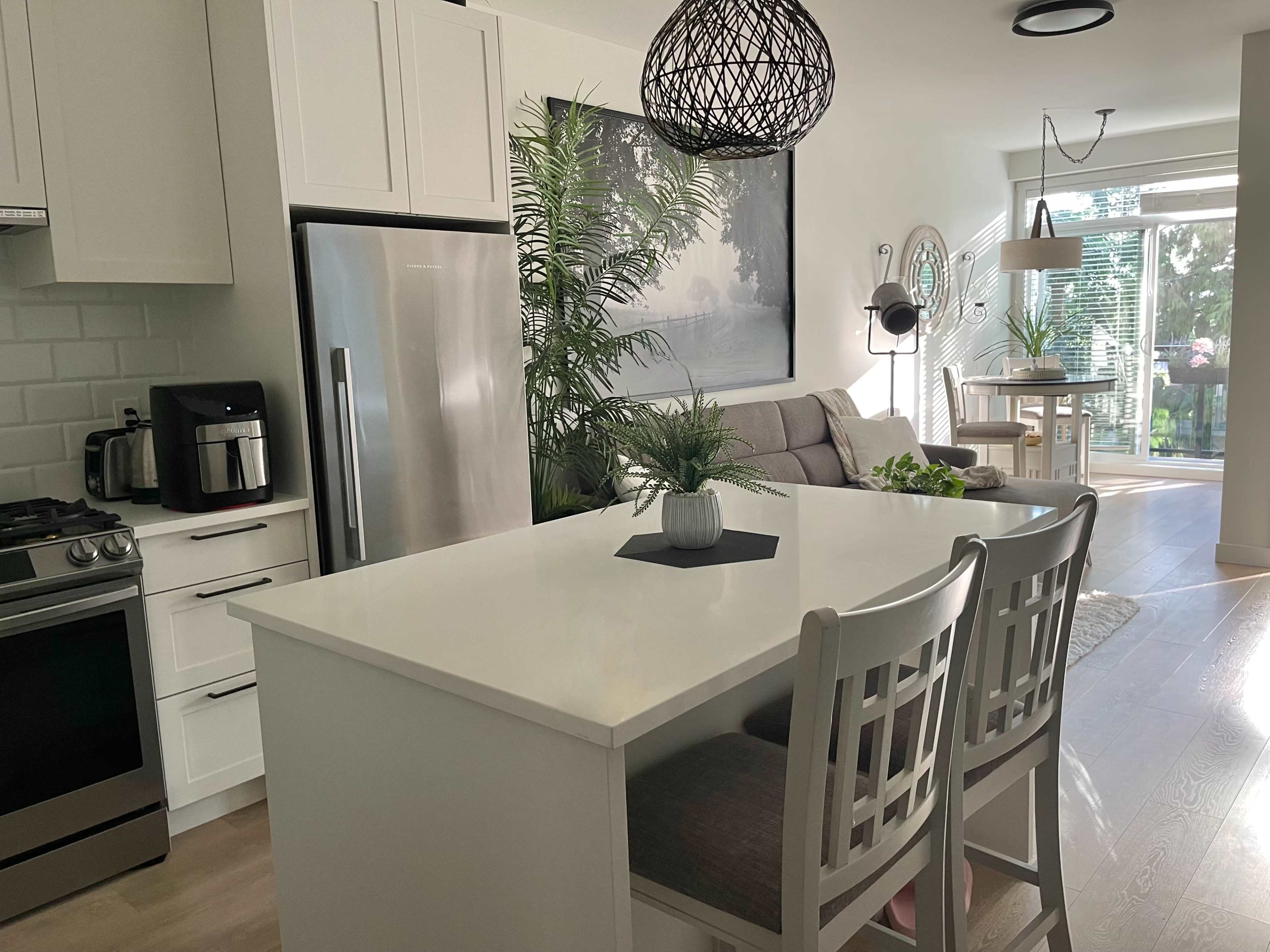 A modern kitchen with a white island, stainless steel appliances, and a dining area that opens to a patio with large windows.