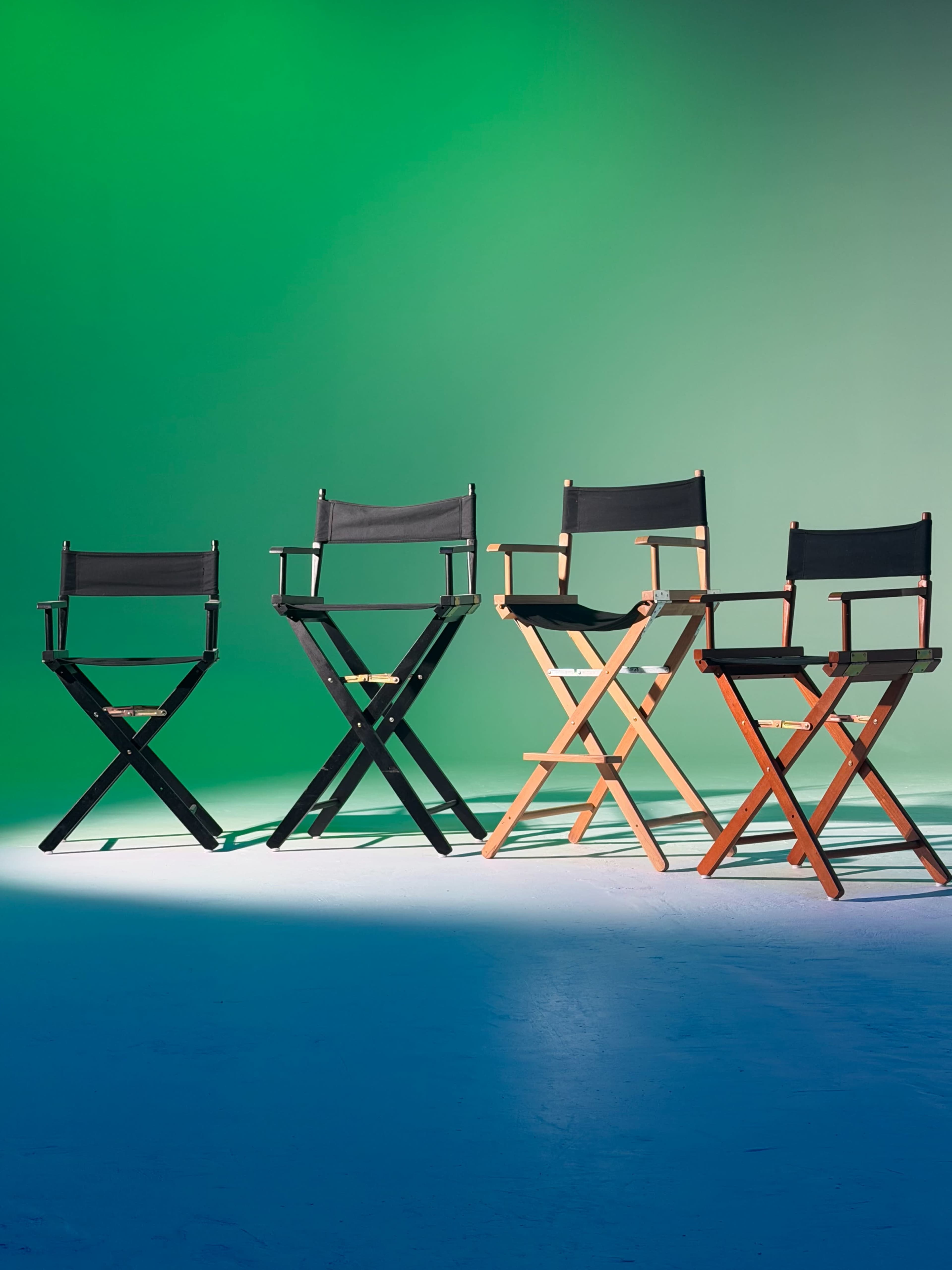 The image shows four director's chairs in a row, each with a different wooden finish, set against a green gradient background.