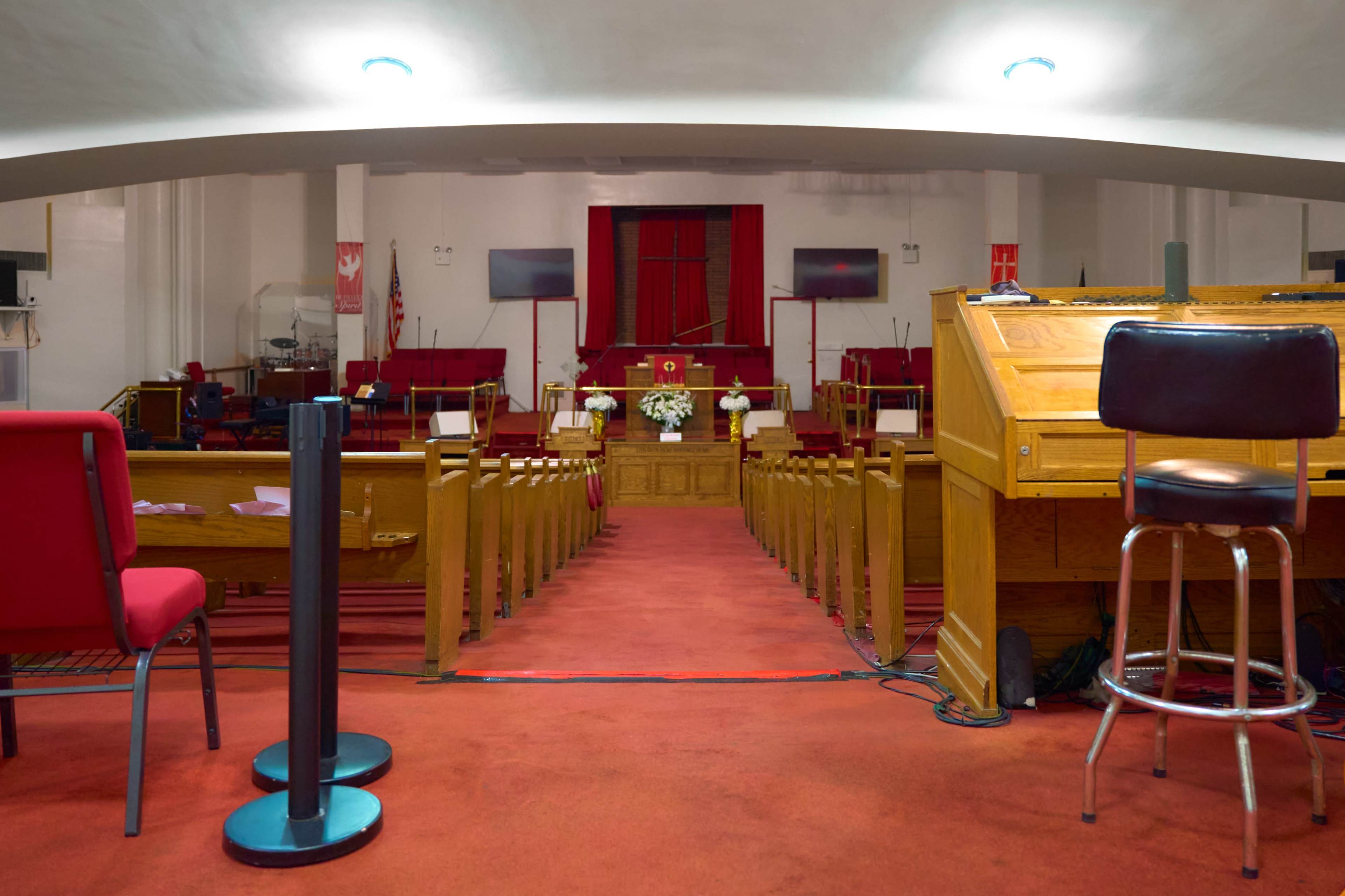 The image shows the interior of a church with red carpeting, wooden pews, and a podium at the front.